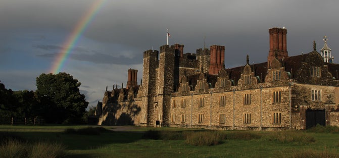 Exterior of historic building, rainbow in dark sky overhead, grass and trees in foreground.