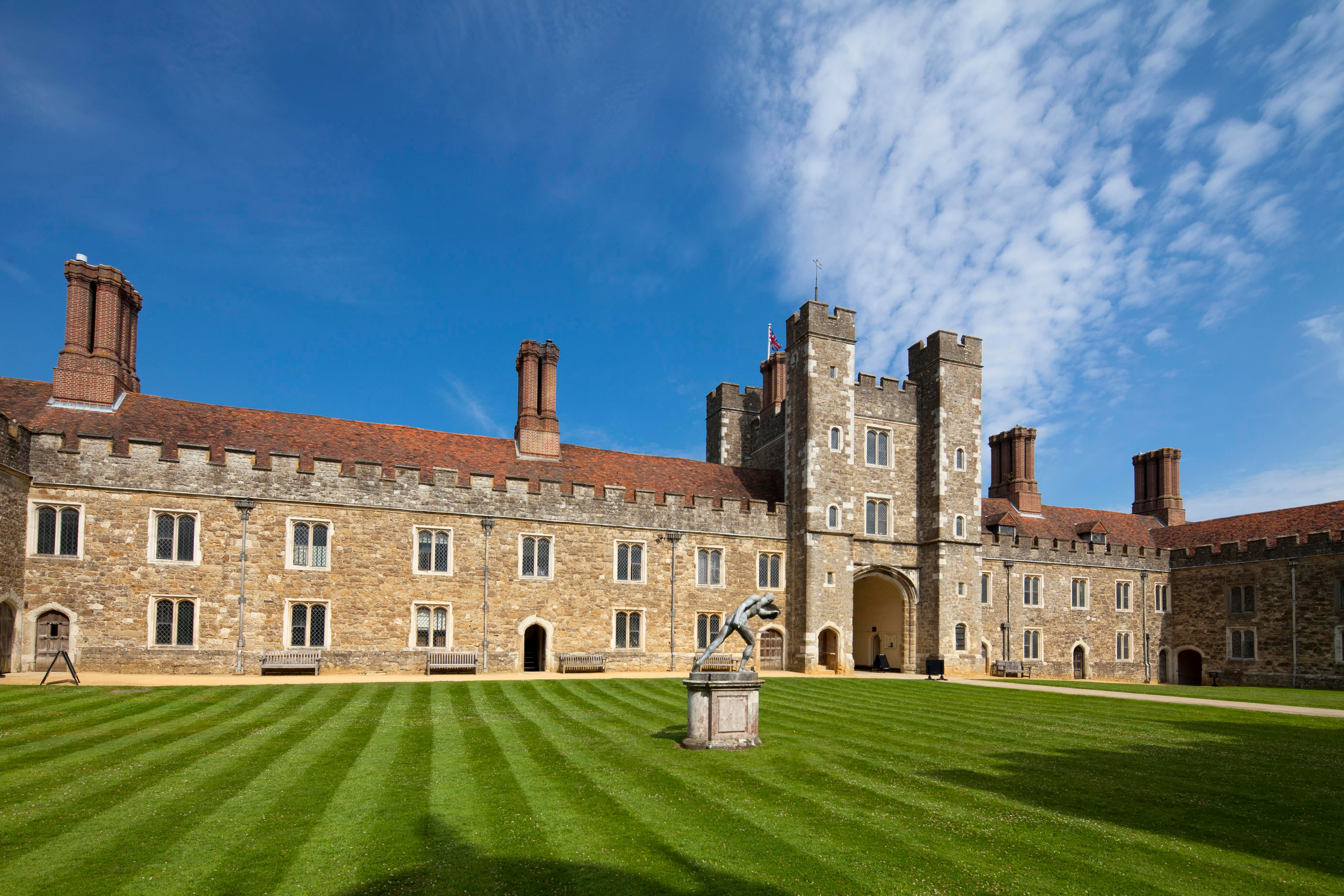 Large old, stone building with bright blue sky above and green grass in front.