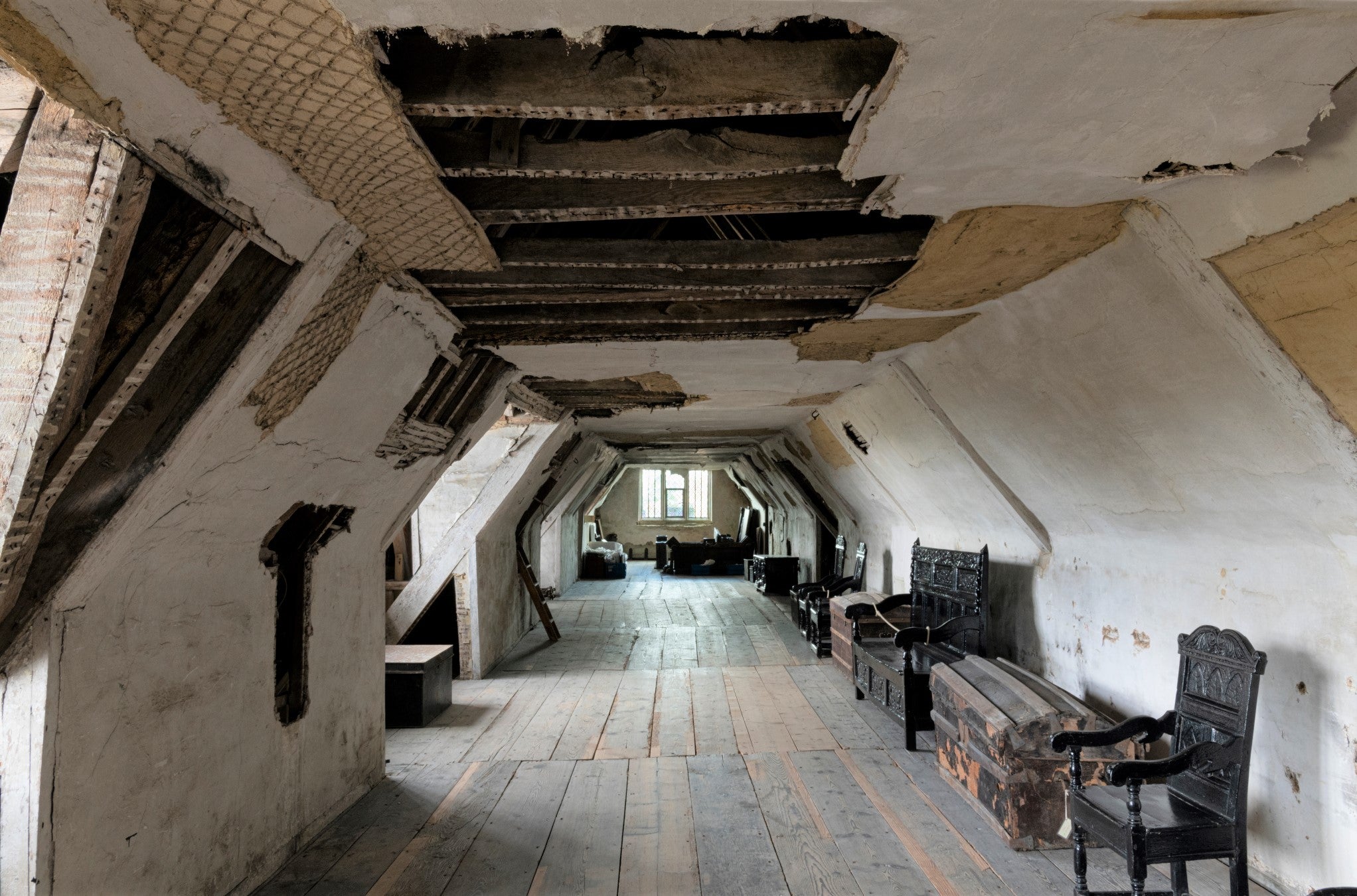 Long view down a covered area with a ceiling with beams showing, wooden floorboards and a window at the end.