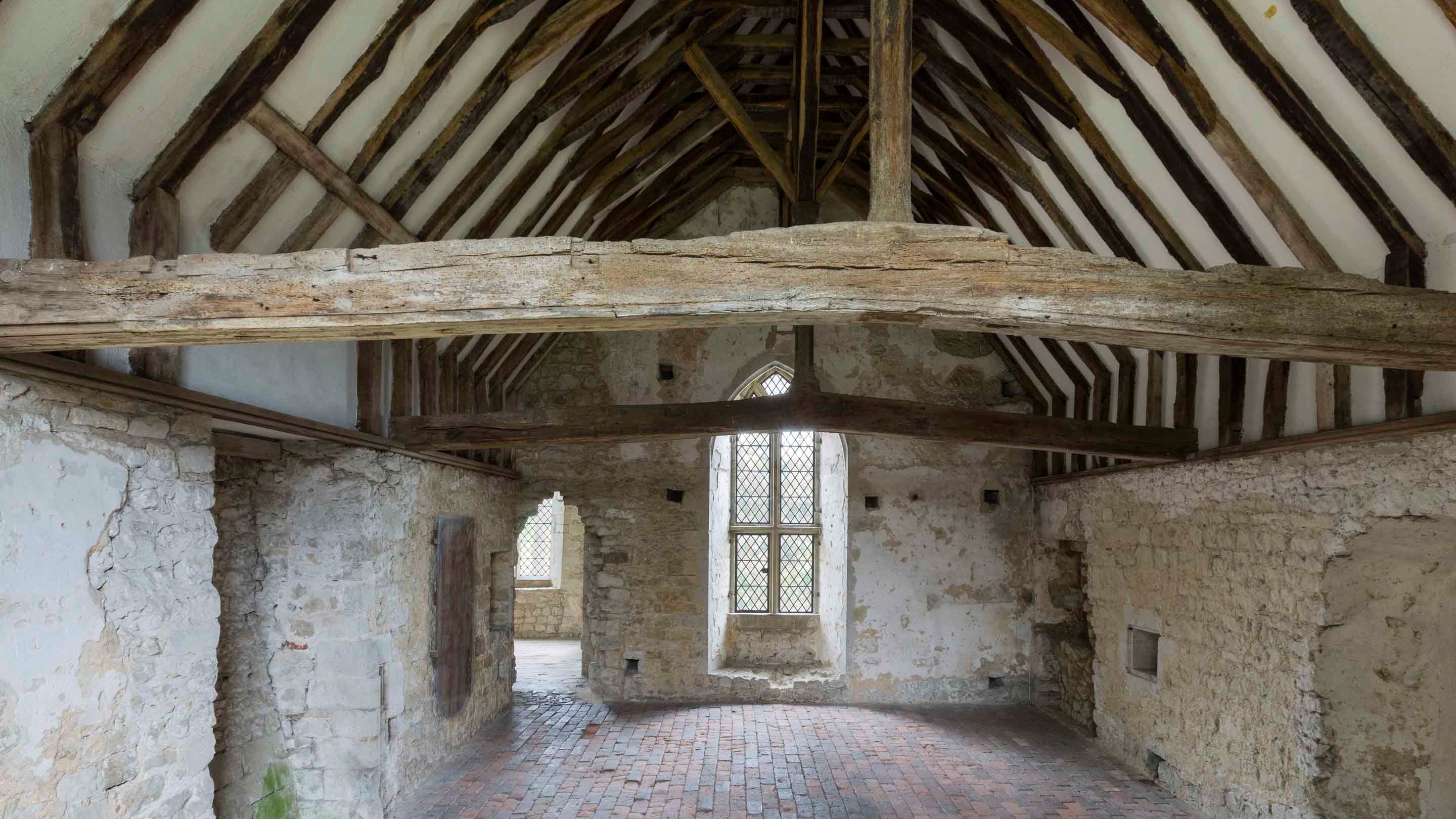 The interior of the Great Chamber or Solar at Old Soar Manor in Kent, showing a steeply pitched and beamed ceiling, stone walls and tiled floor.