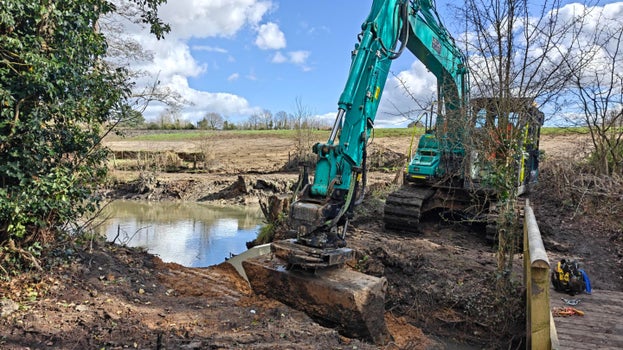 Image of an excavator working to create an outflow stream from Flushers Pond on a sunny day