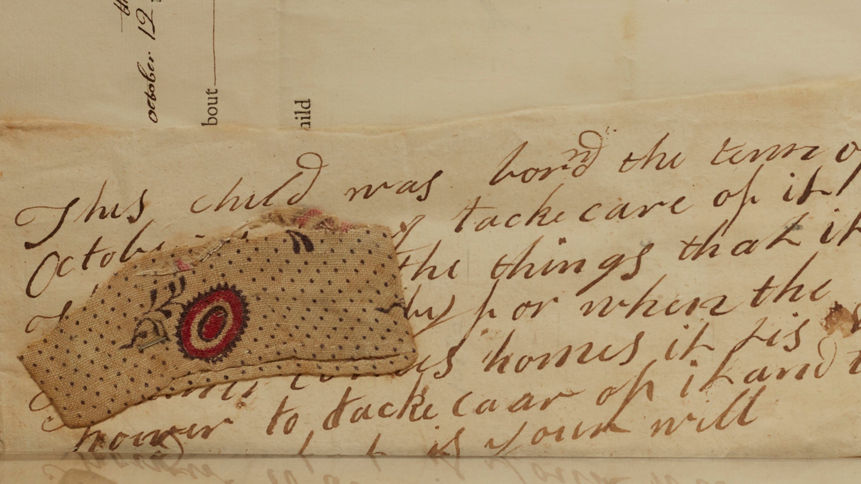 A Coram Foundling Hospital Token. a piece of fabric with a red and blue flower and blue polka dots pinned to a hand written note asking to take care of the child left in the care of the Westerham Foundling Hospital.