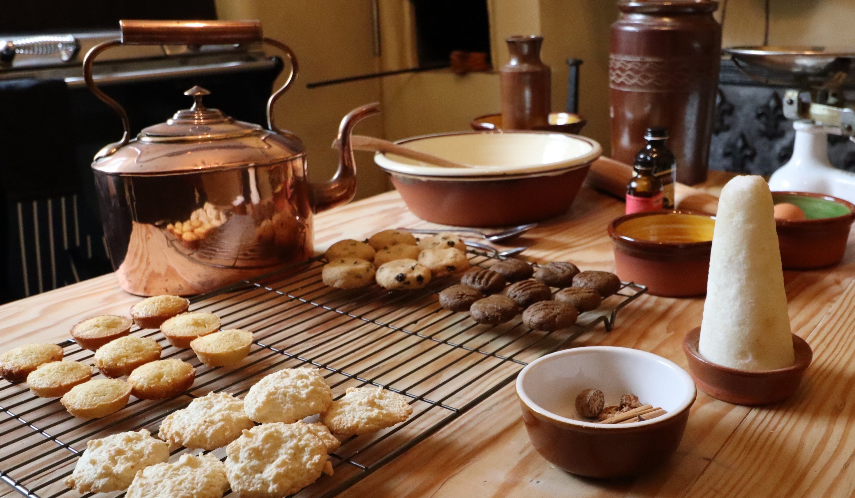 Copper kettle, trays of baked cookies, bowl of cinnamon, pillar of sugar, baking equipment in Quebec House Georgian kitchen