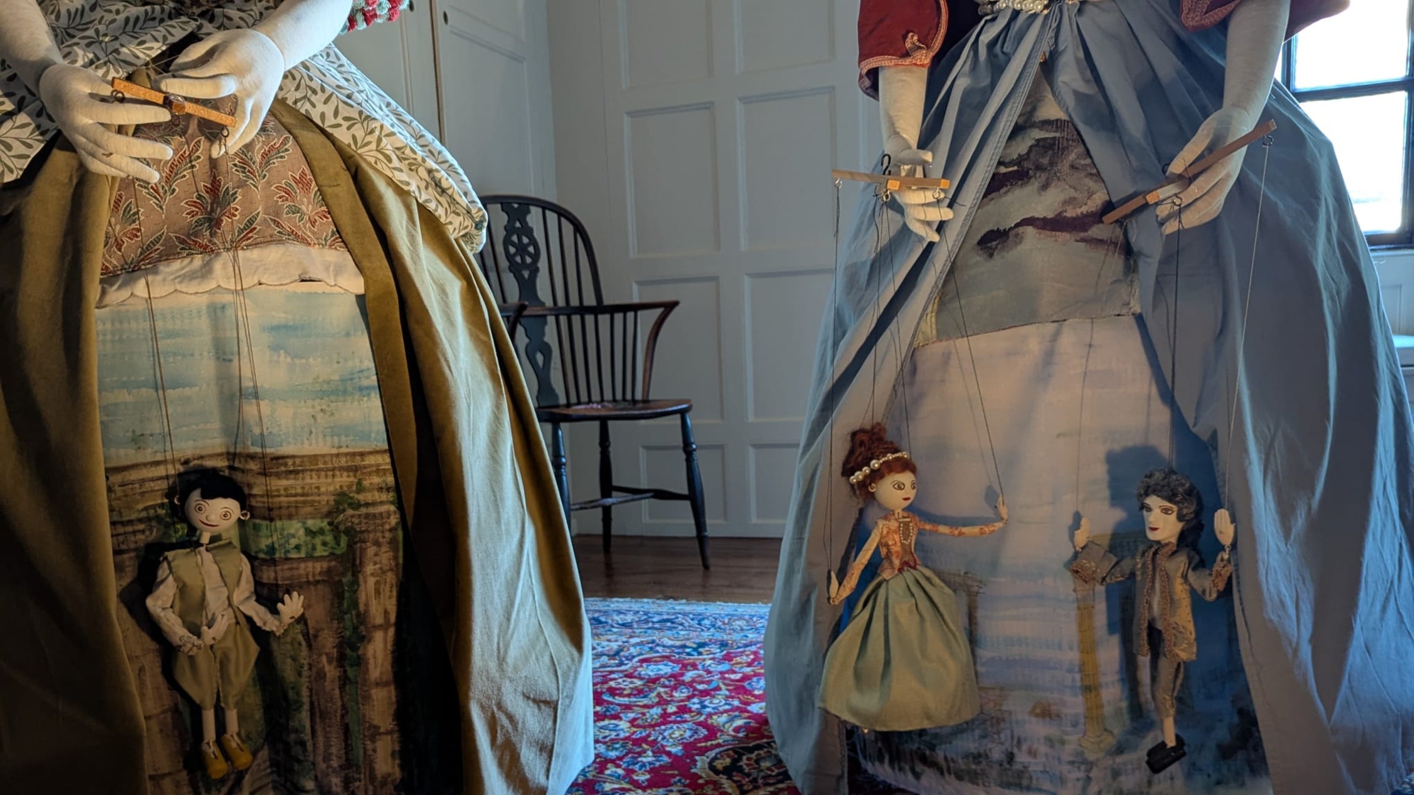 Marionette figures in the skirts of Georgian Dresses. One is a poor young man from the country with a woodlands background, the others are a young woman speaking with an aristocratic gentleman.