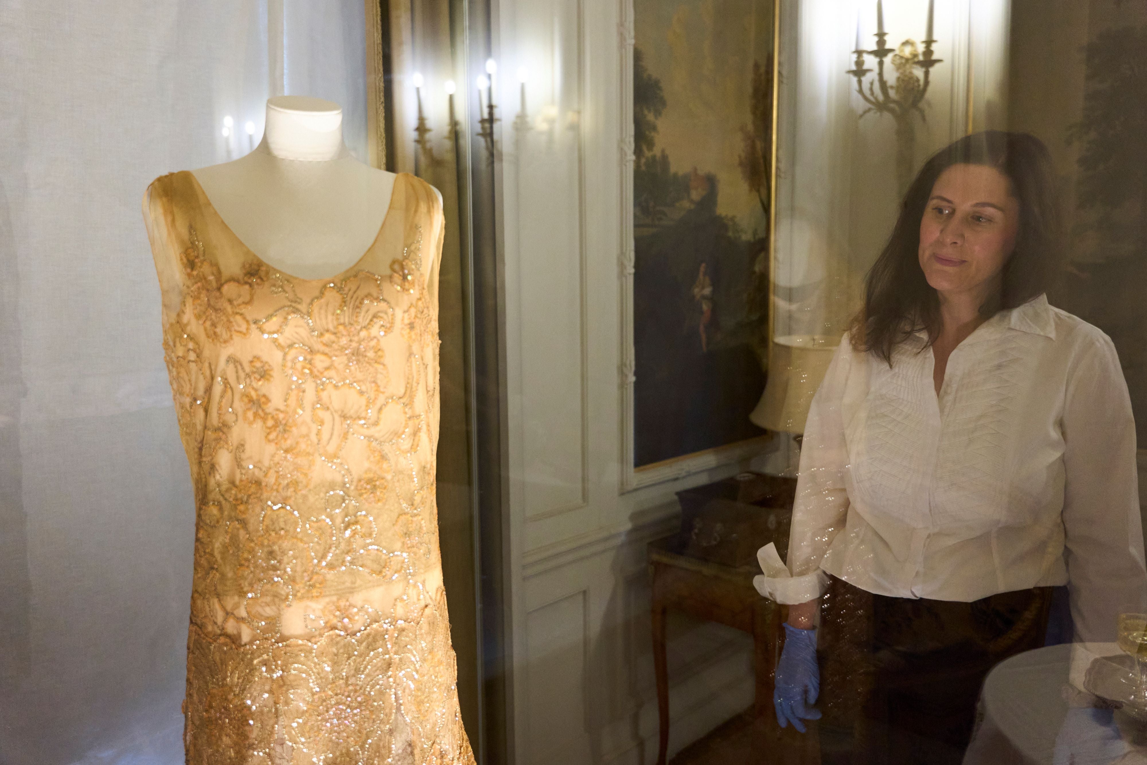 A woman looks at a dress on a mannequin in a glass case