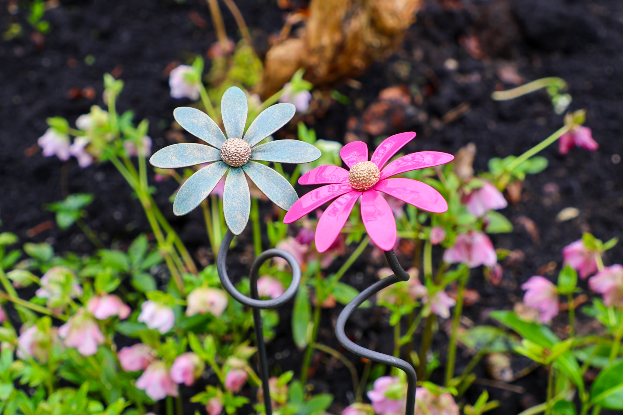 Two steel daisies stand next to each other against greenery