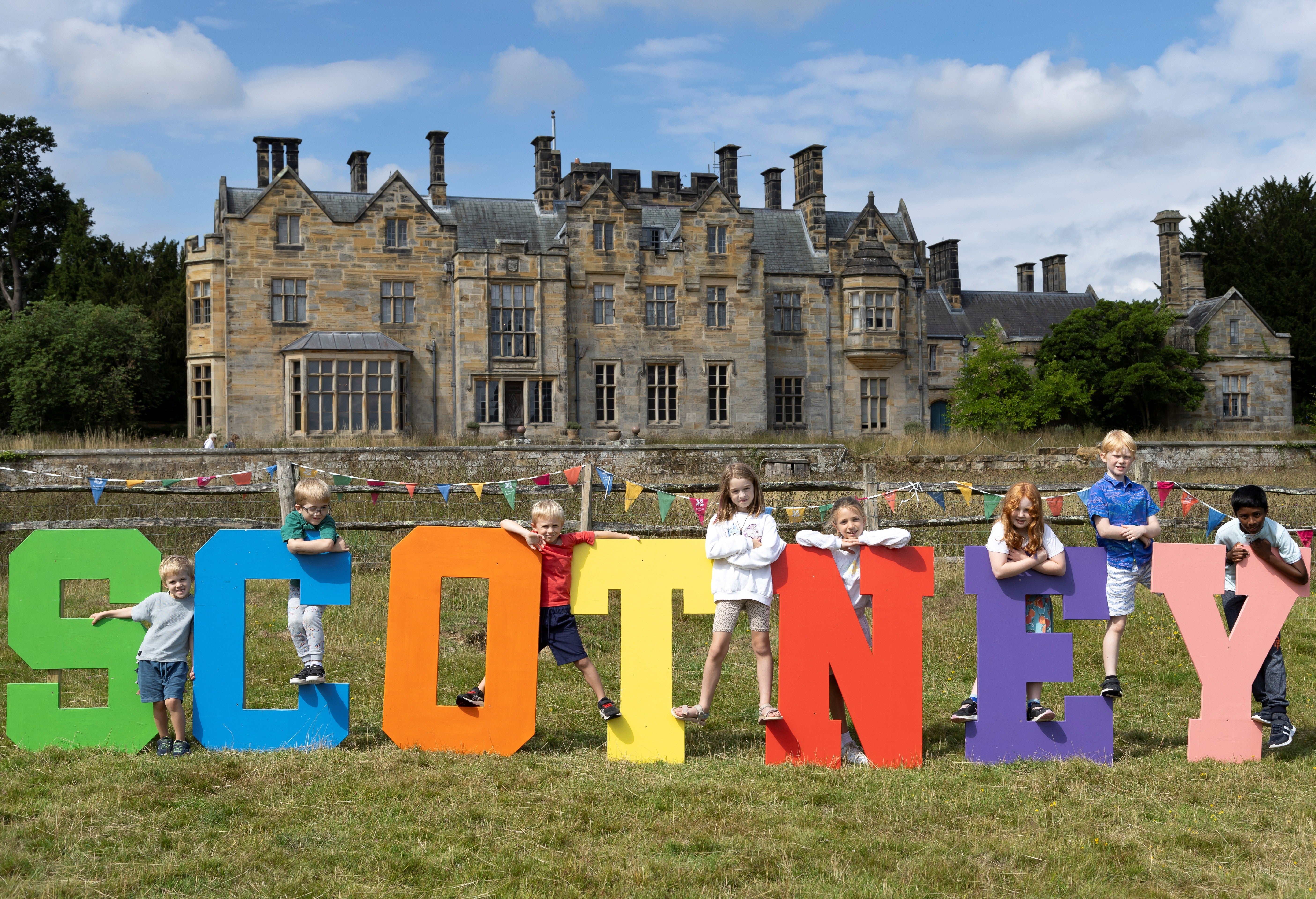 Eight children posing on the colourful SCOTNEY letter at the Summer of Play event at Scotney Castle, Kent