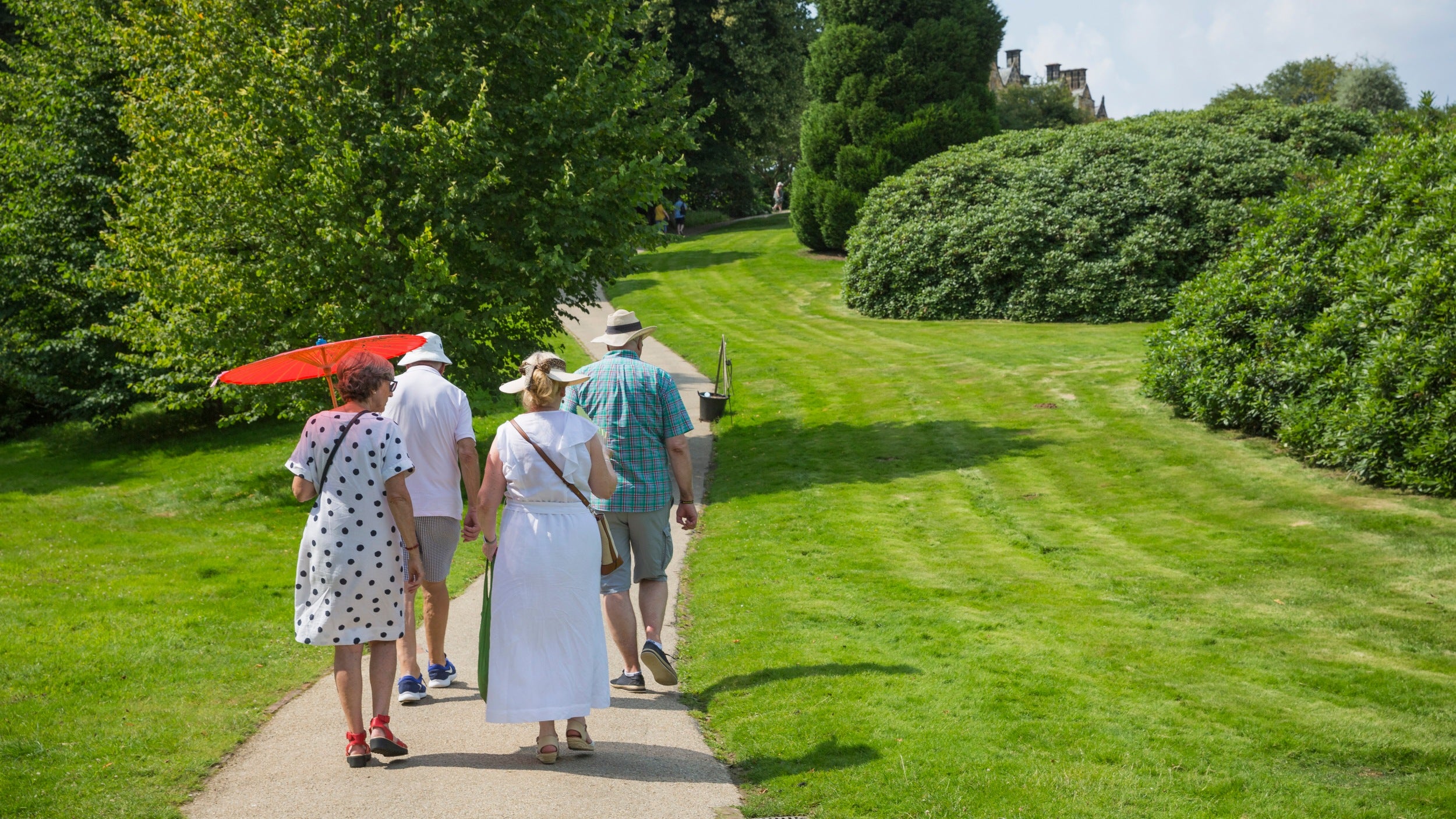 A group of adults walking along a path between mowed grass gardens and trees