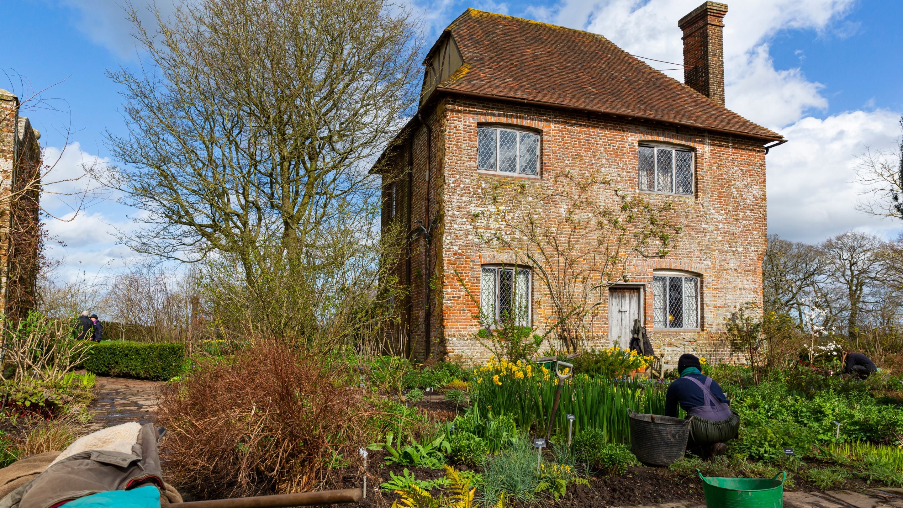 Gardener at work, kneeling in a flowerbed in the South Cottage garden at Sissinghurst Castle Garden, Kent