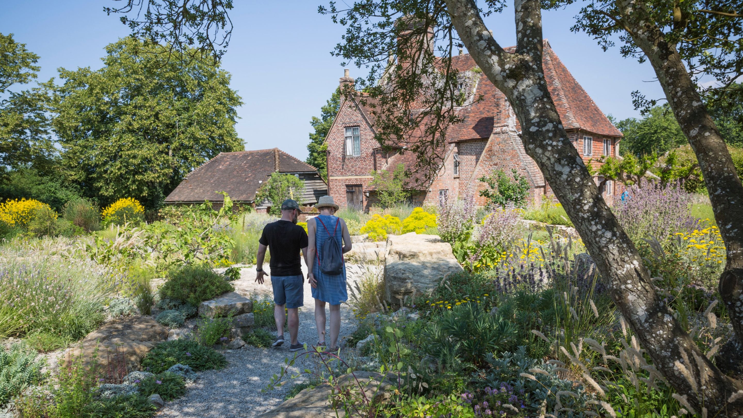 Two visitors, one male, one female in the newly re-created Delos garden in summer at Sissinghurst Castle Garden, Kent