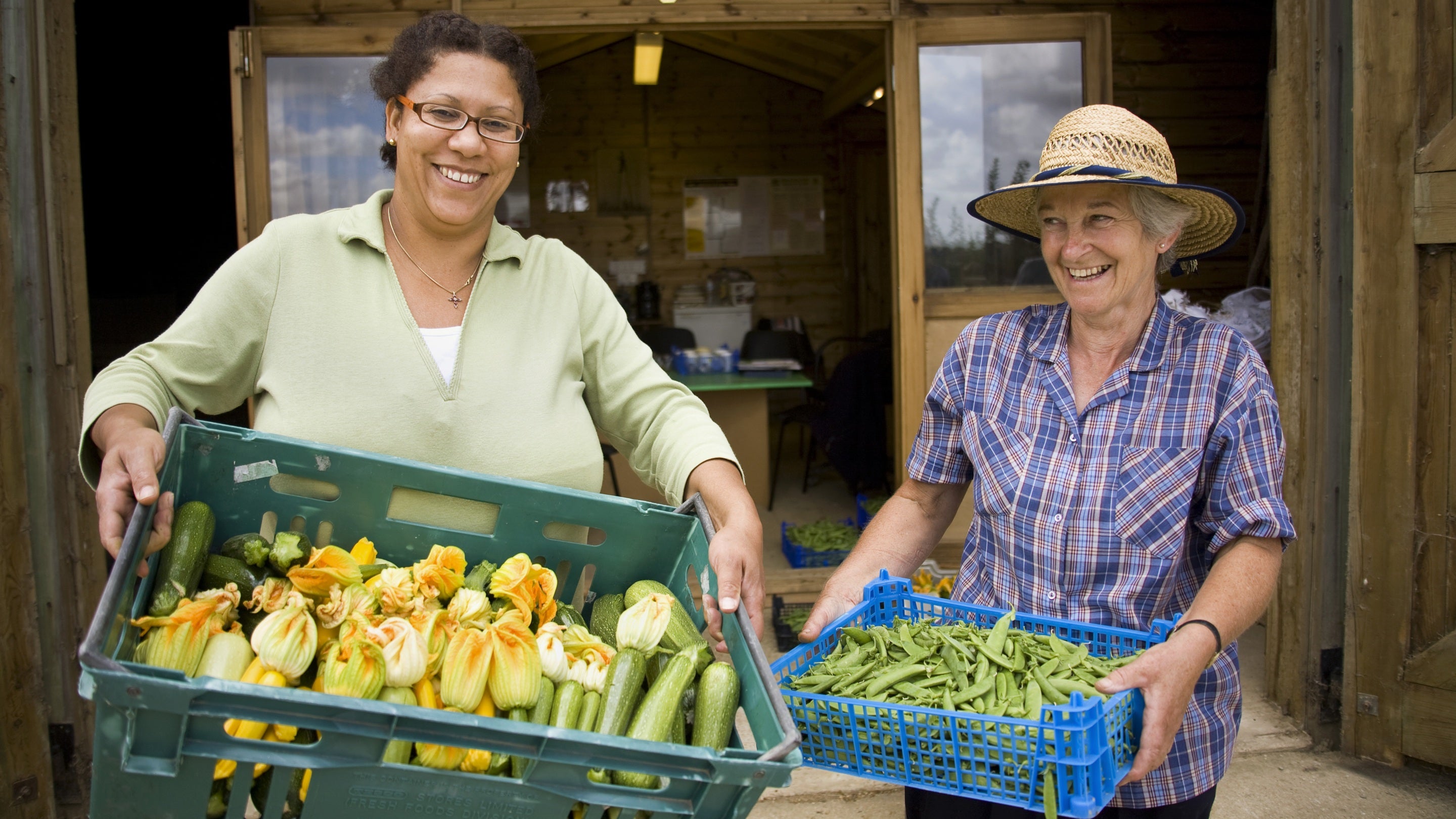 Two female volunteers hold crates of vegetables they've picked for use in the kitchen at Sissinghurst Castle Garden, Kent