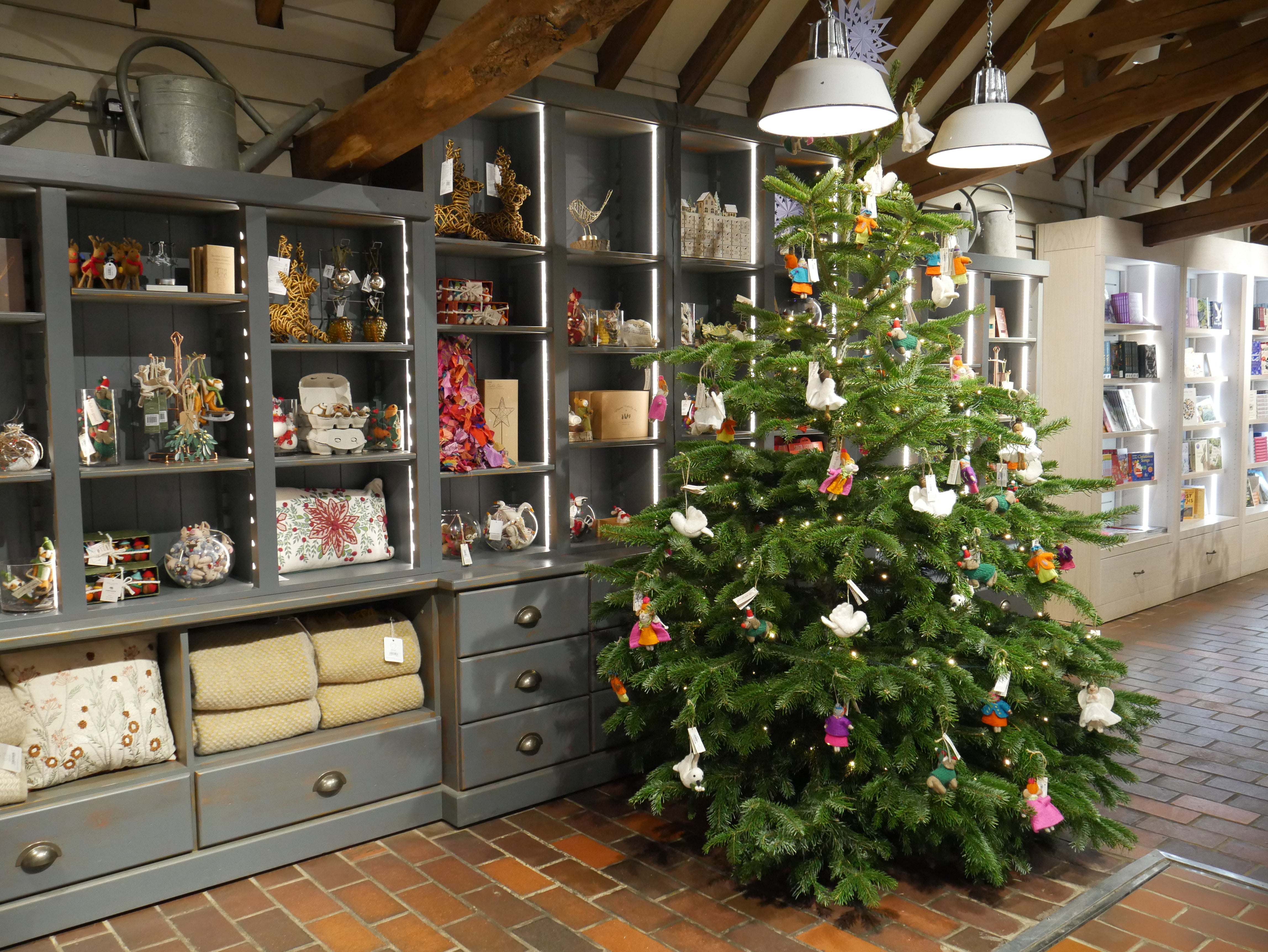 A Christmas tree stands in the middle of a shop floor, decorated with felt animals, with filled shelves behind it