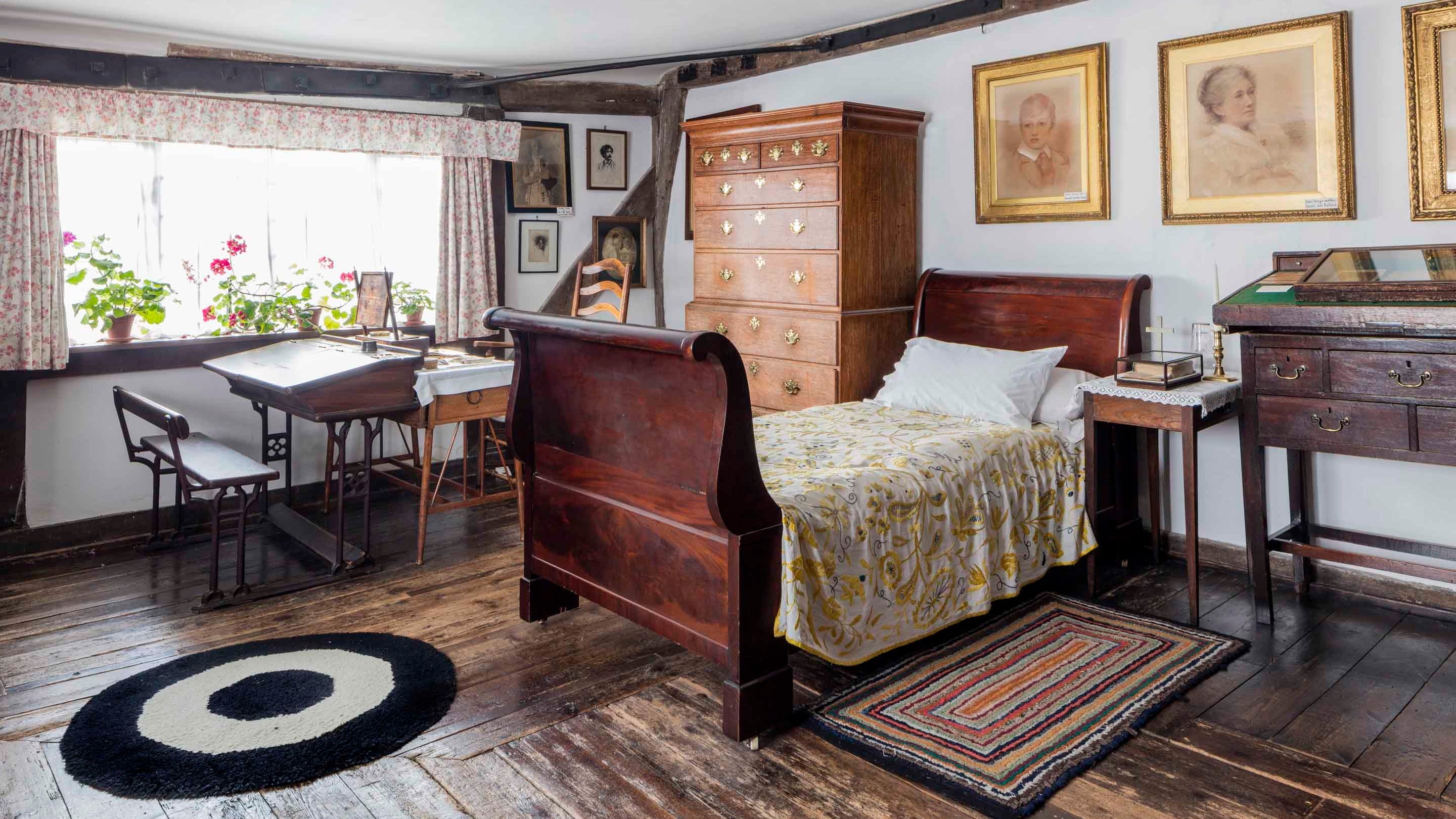 The bedroom at Smallhythe Place showing an antique bed, desk, benches, storage furniture and rugs on a wooden floor.