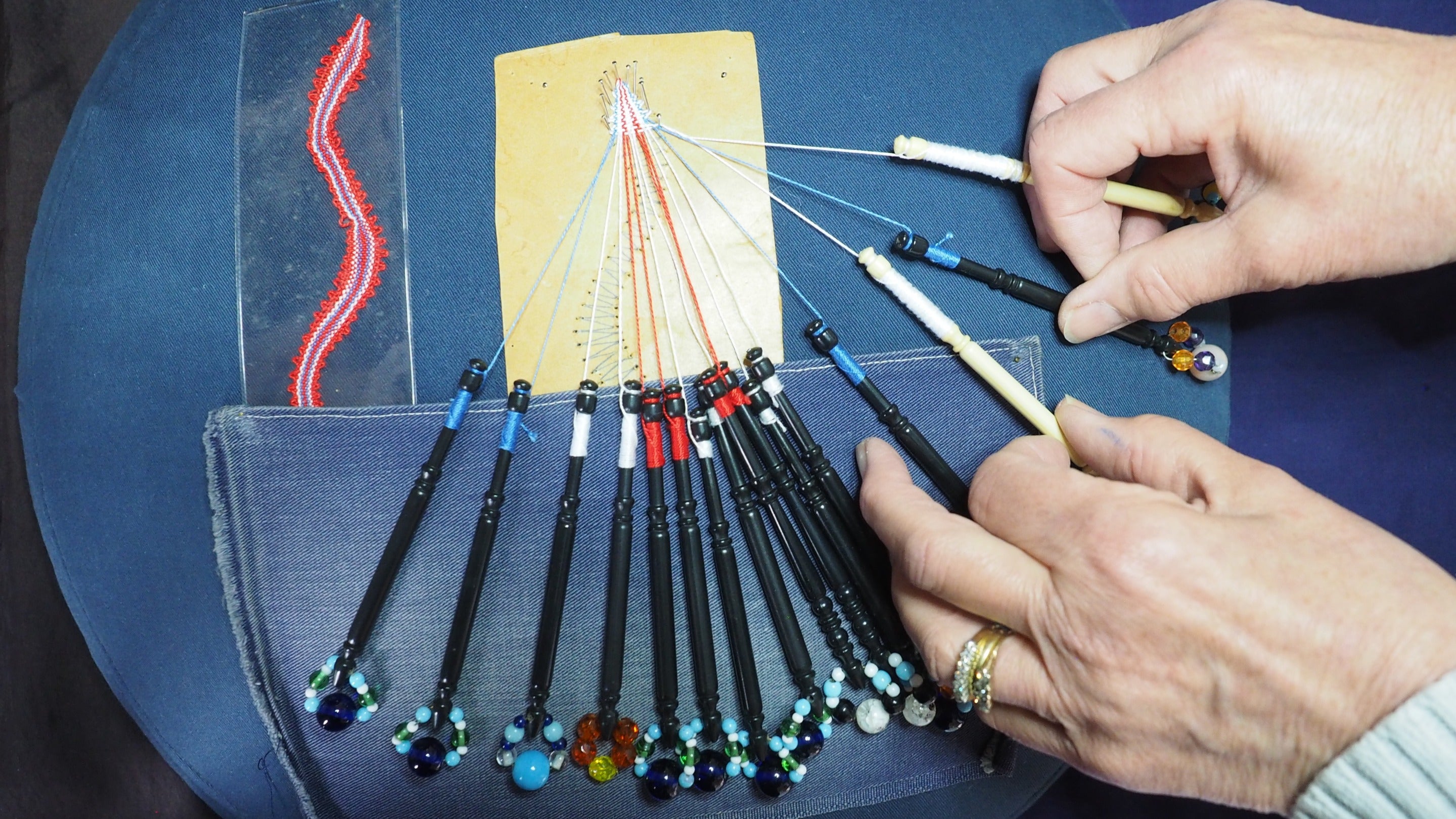 Image of a lace pillow with many bobbins and multicoloured threads on a blue background