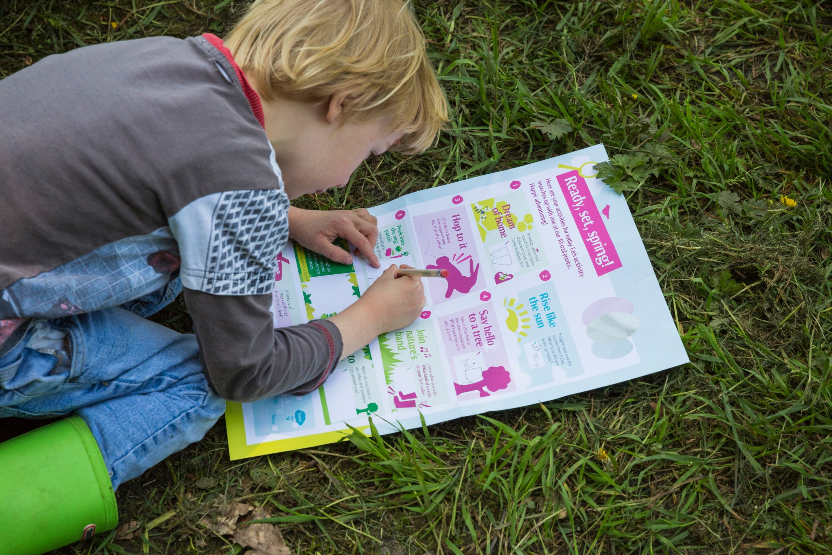 Image of a child wearing wellington boots, kneeling on grass, completing their Easter trail sheet