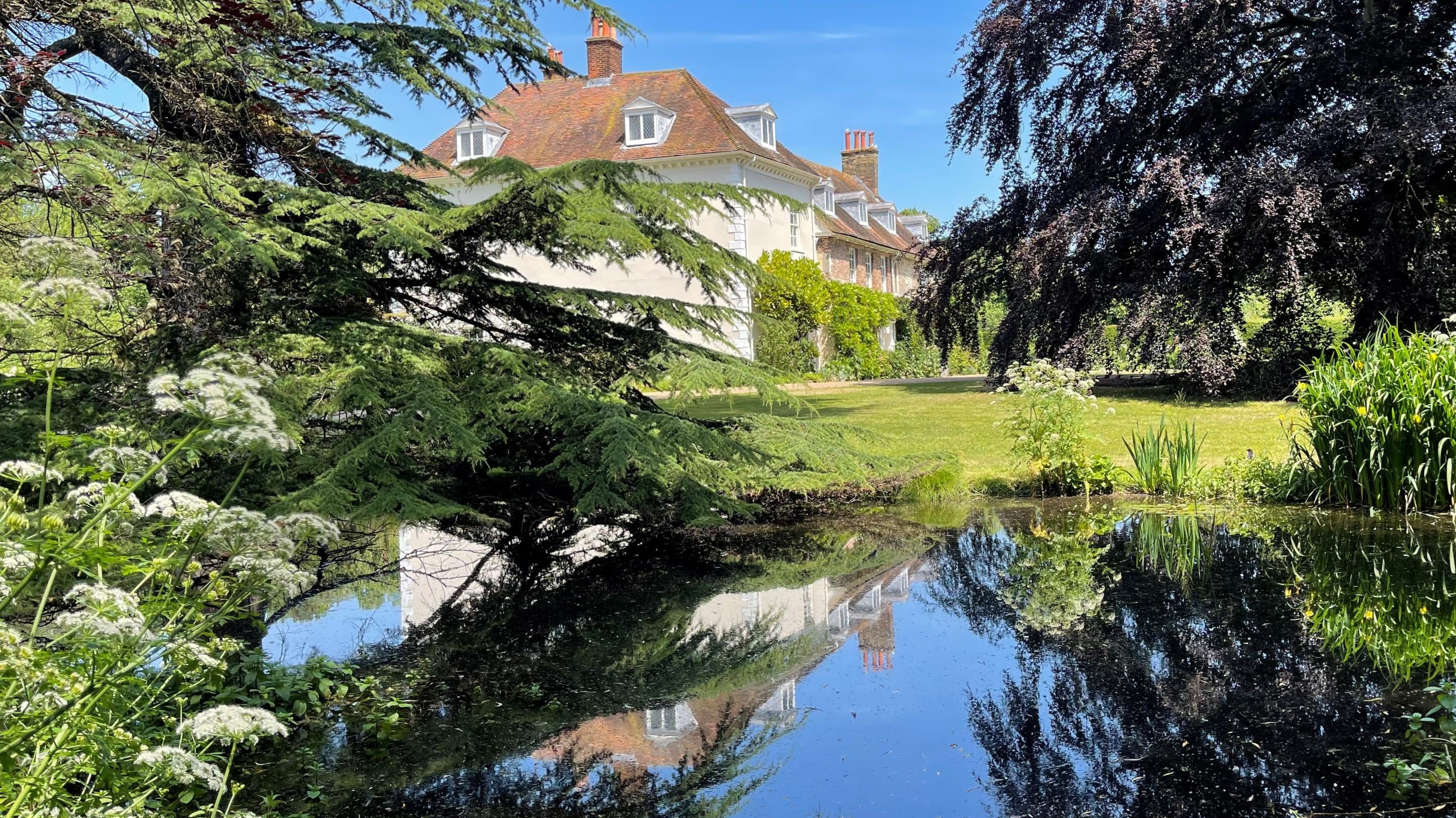 Image of the St John's Jerusalem house and chapel from the river with a reflection in the water and blue sky.