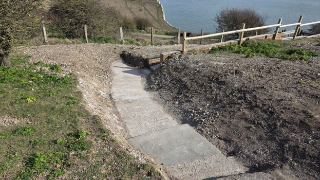 An image of a path with steps leading down a hill with the White Cliffs of Dover and the sea in the background