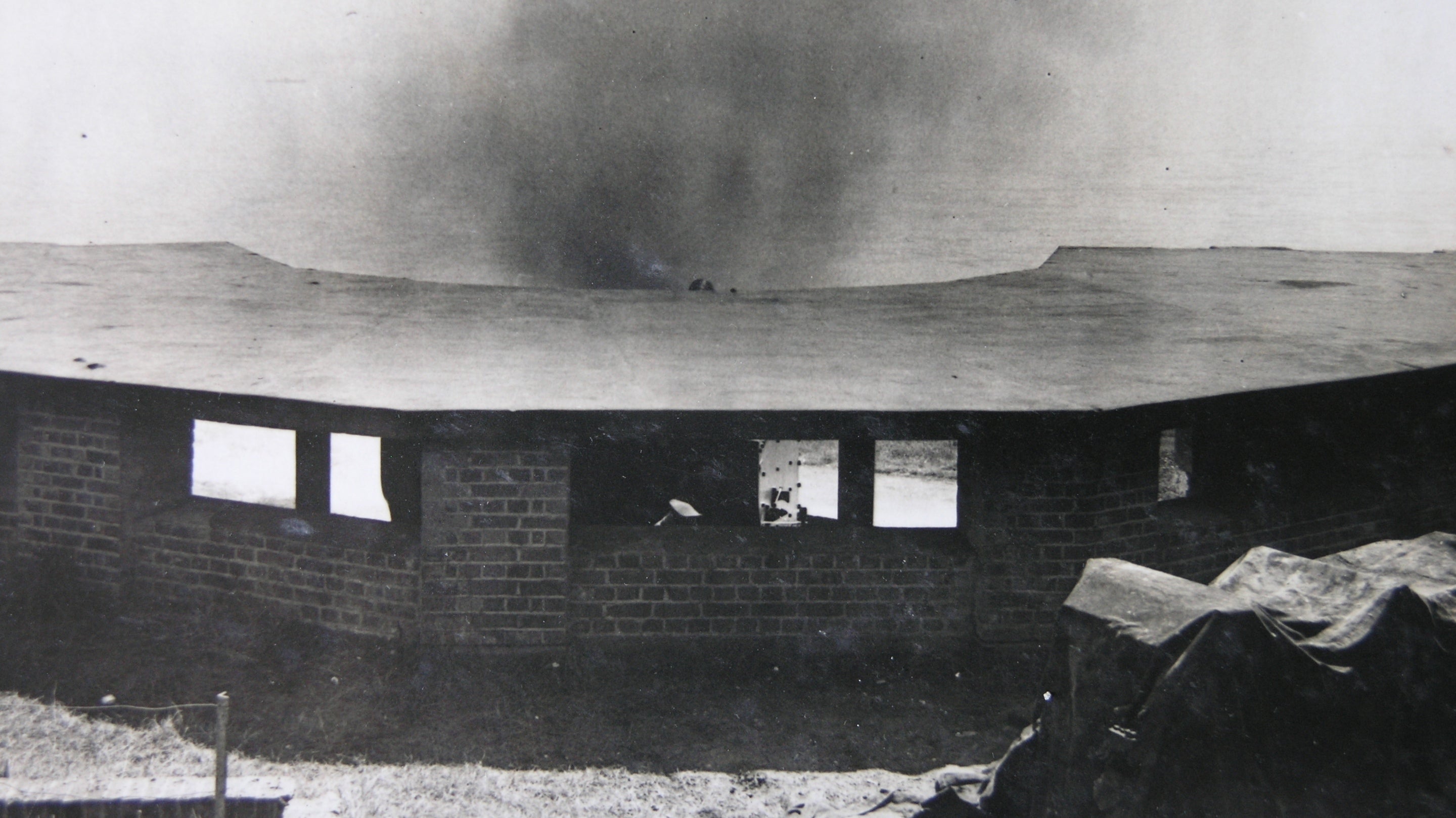 Black and white image of a brick gun emplacement with smoke from firing