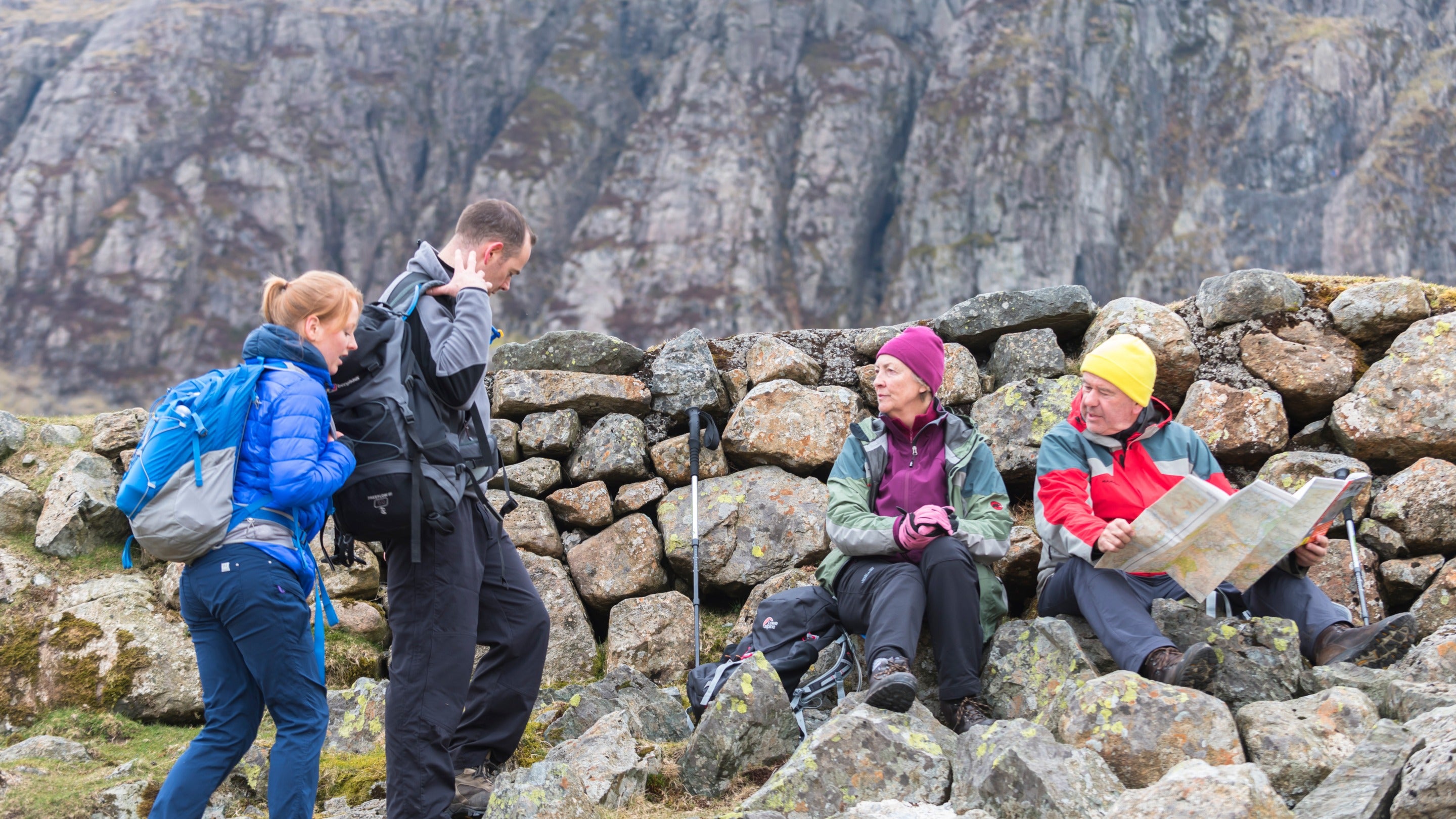 Walkers resting against a dry stone wall on the fellside at Stickle Ghyll, Cumbria