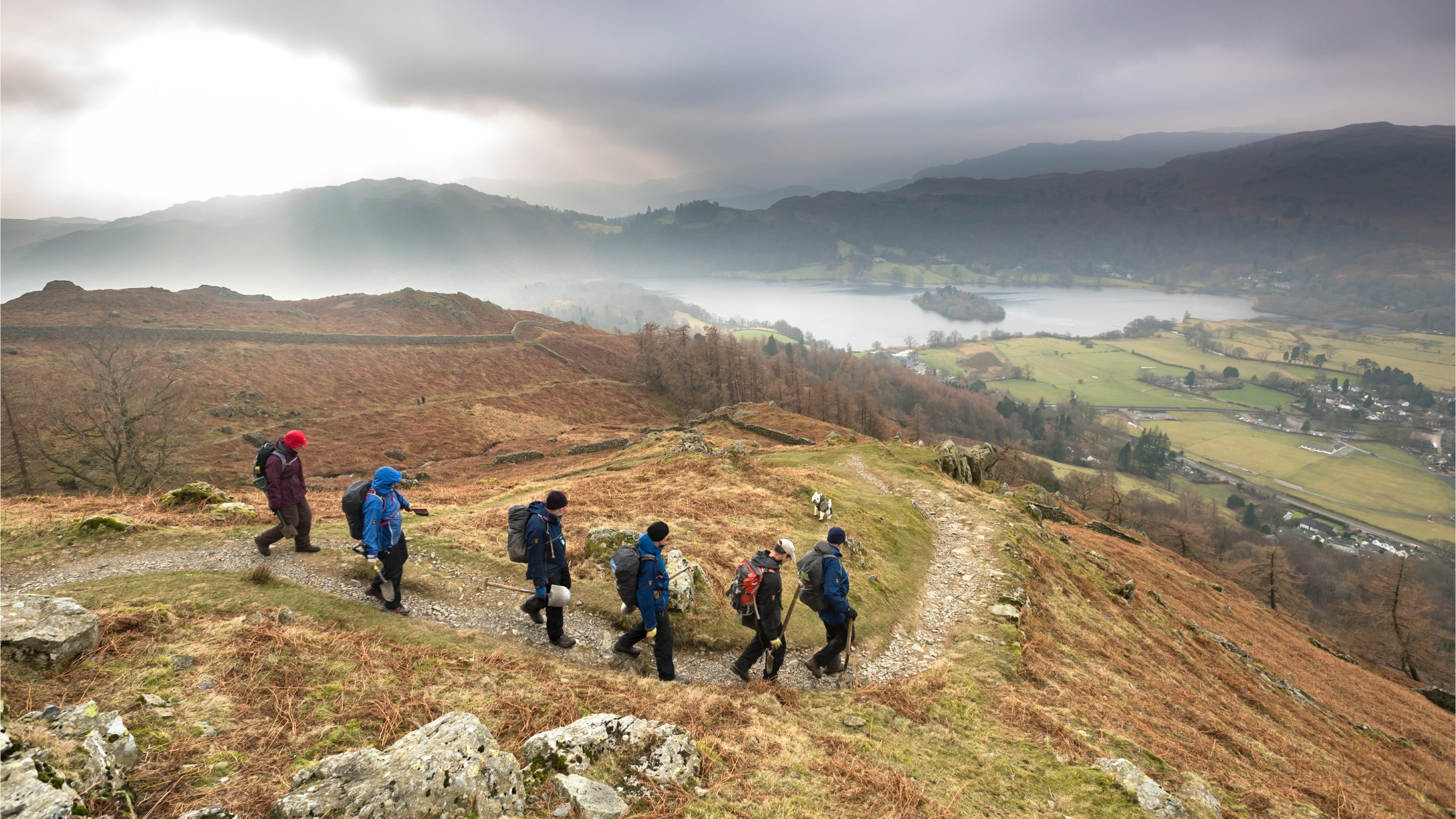 Walkers descending a path down the side of a fell towards the lake in Grasmere, Cumbria