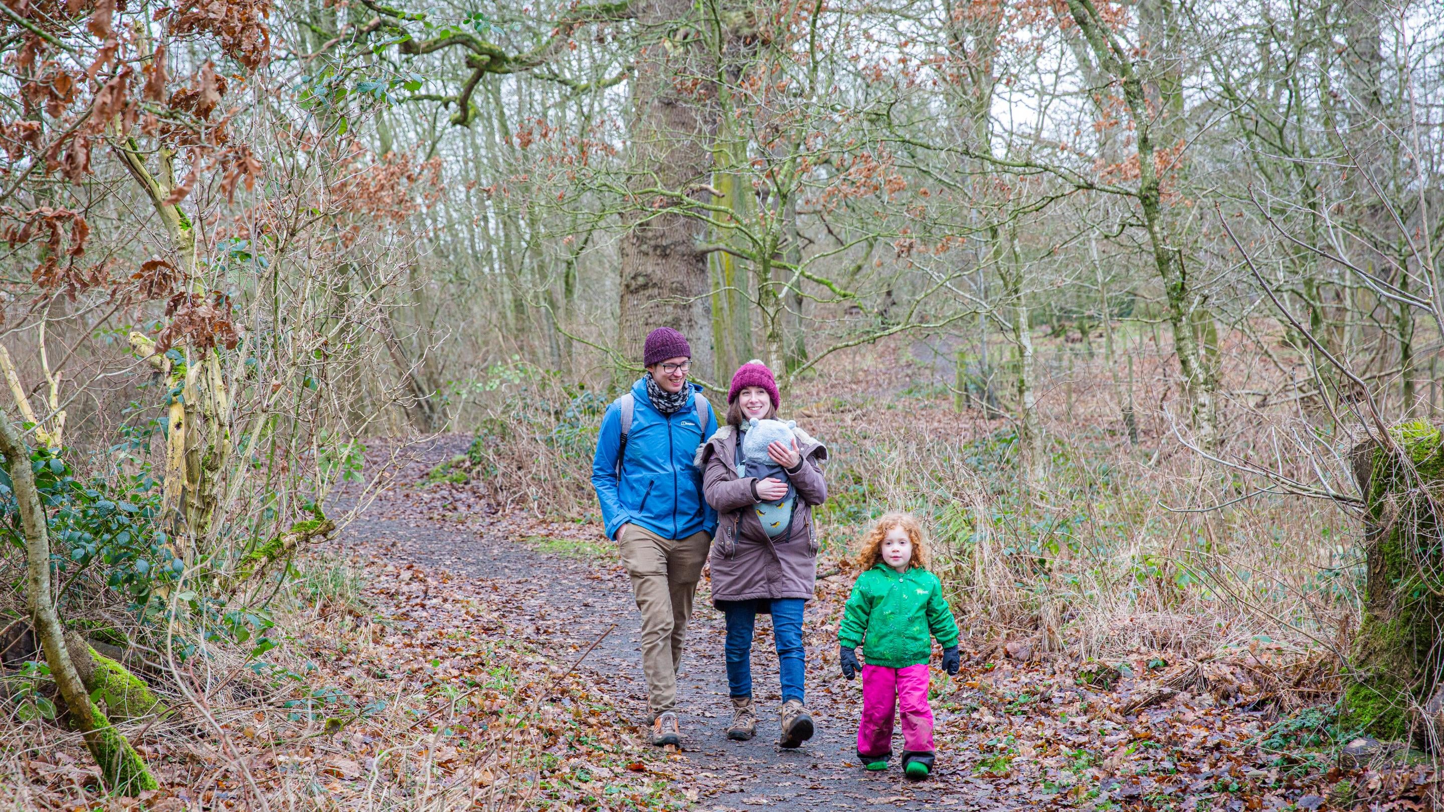 A family walking through woodland in winter at Acorn Bank, Cumbria