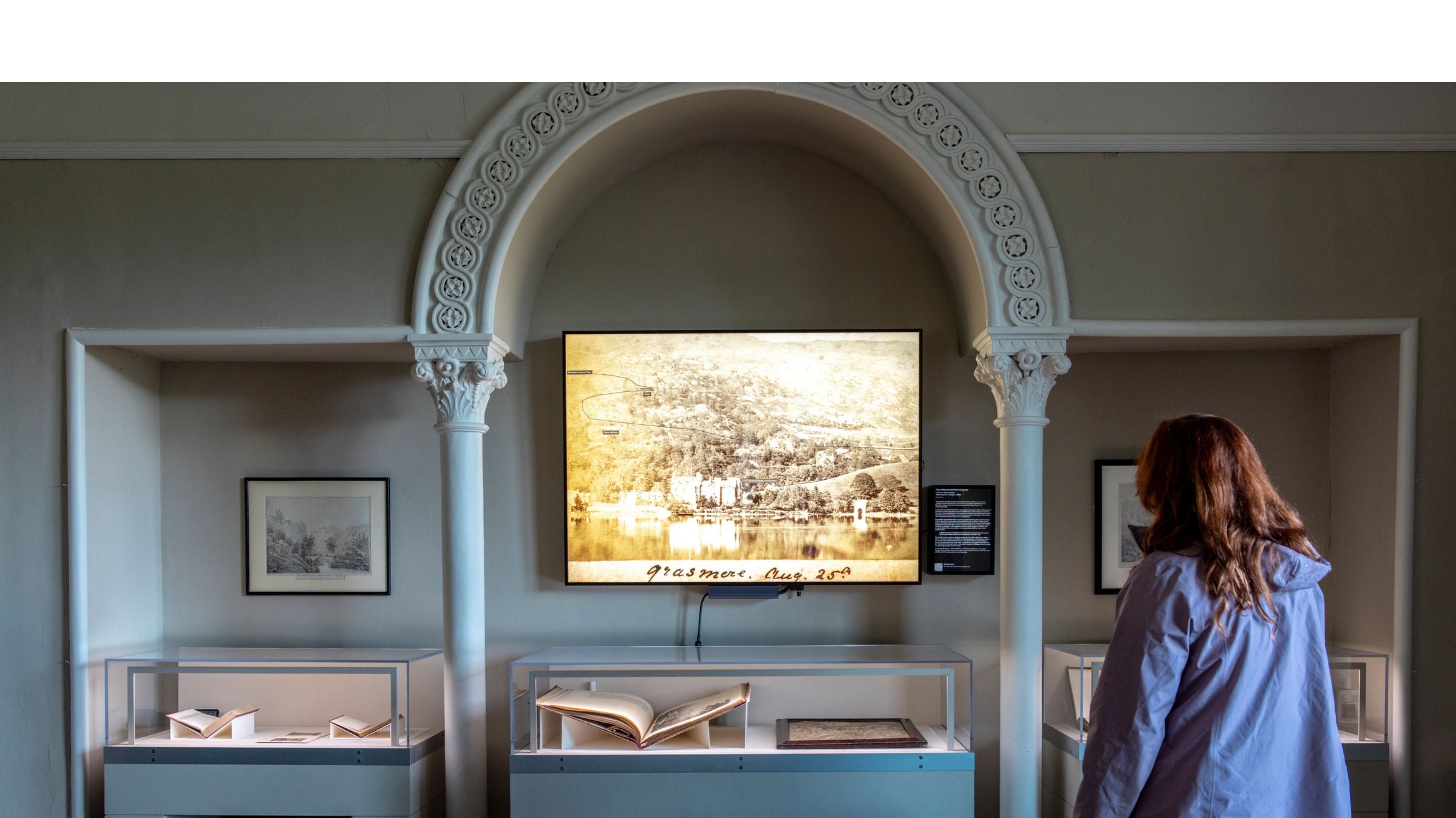 Visitor viewing historical exhibition at Allan Bank, Grasmere, featuring archival photographs and documents.