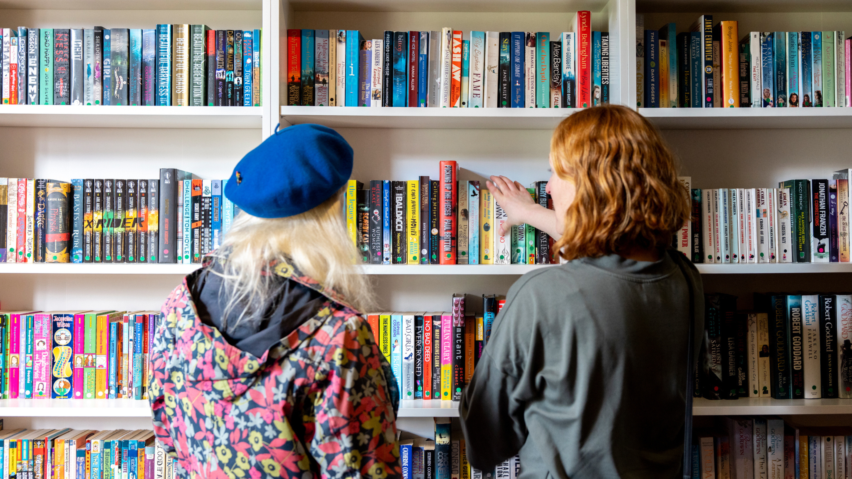 The backs of two people stood looking at selves filled with books.