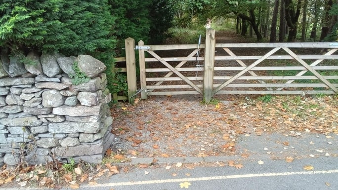 A wooden gate next to a stone wall and hedge with an area of footpath in front of it, Allan Bank and Grasmere, Cumbria