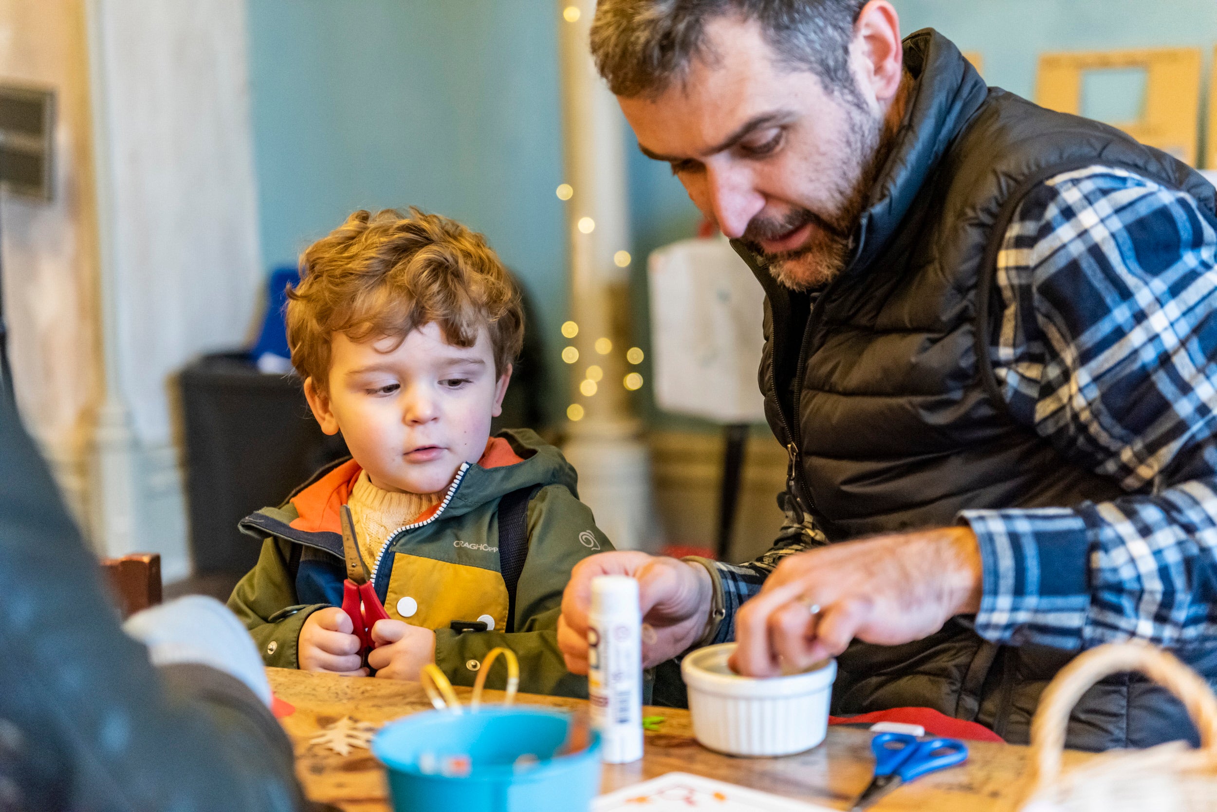 Young boy and father sat together at table doing Christmas craft activities.