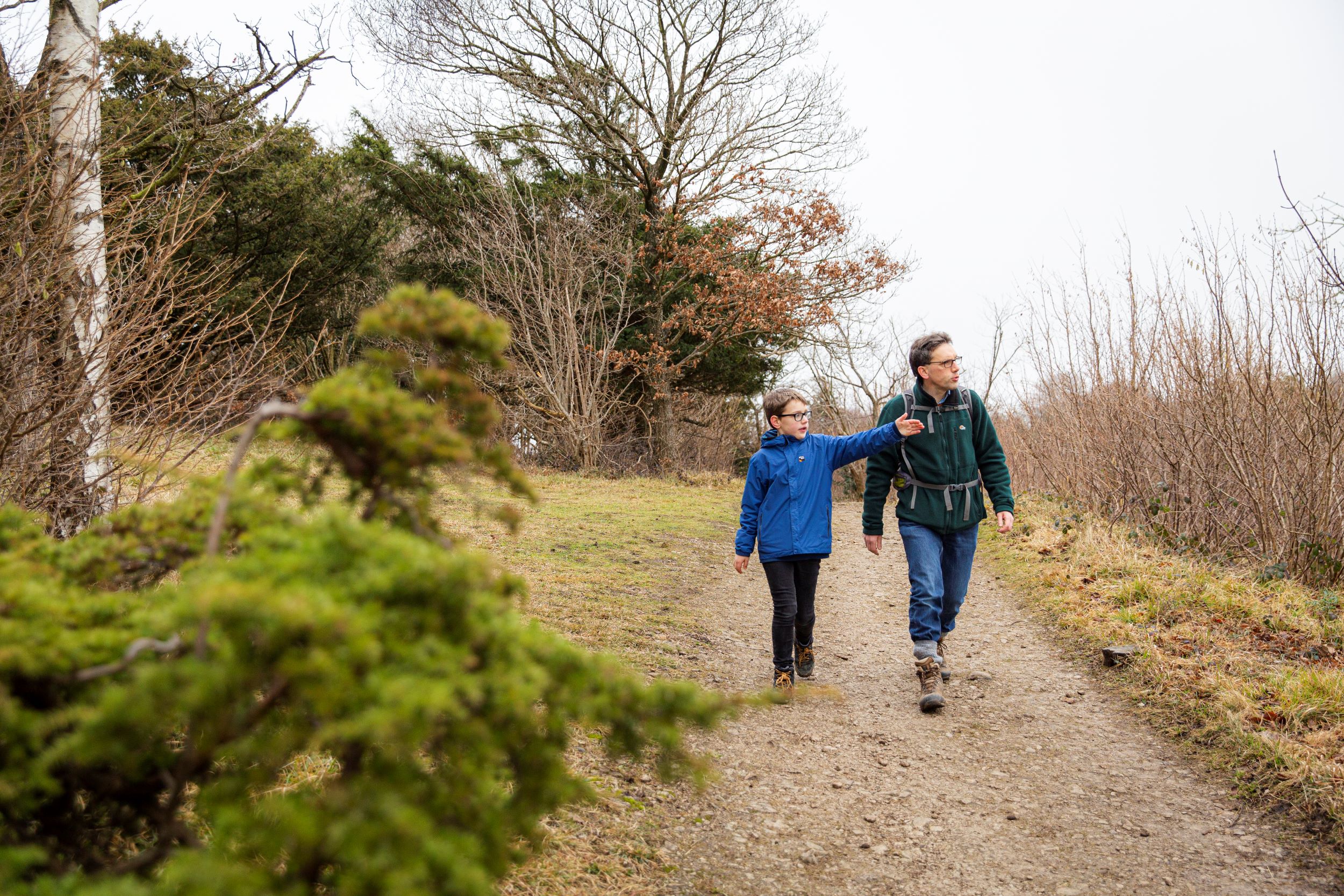 Child wearing glasses and a blue raincoat walking with his father, who has a green coat and a rucksack on, at Arnside and Silverdale.