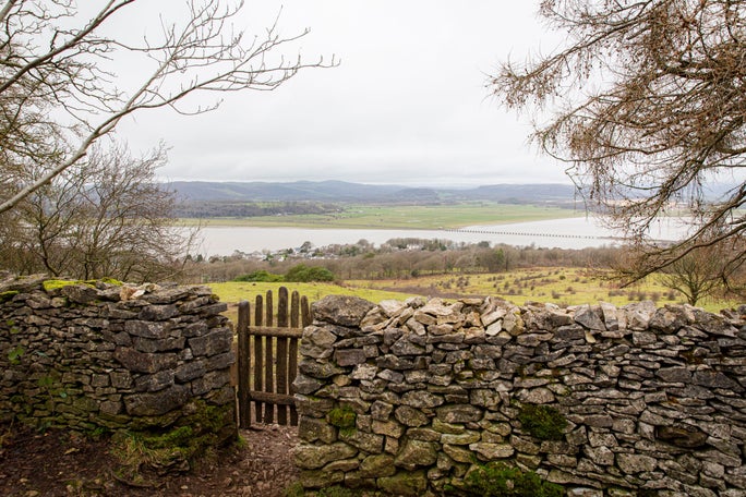 A wooden gate in a dry stone wall, with a view out over the estuary, on a grey day at Arnside and Silverdale.