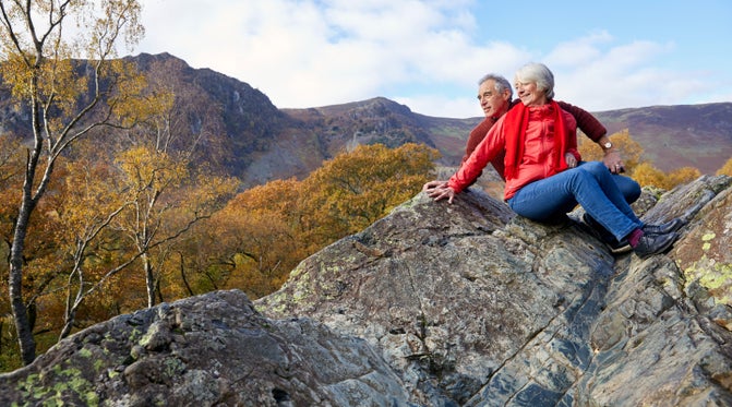 A couple sits enjoying the view from the top of the Bowderstone in Borrowdale on a sunny Autumn day