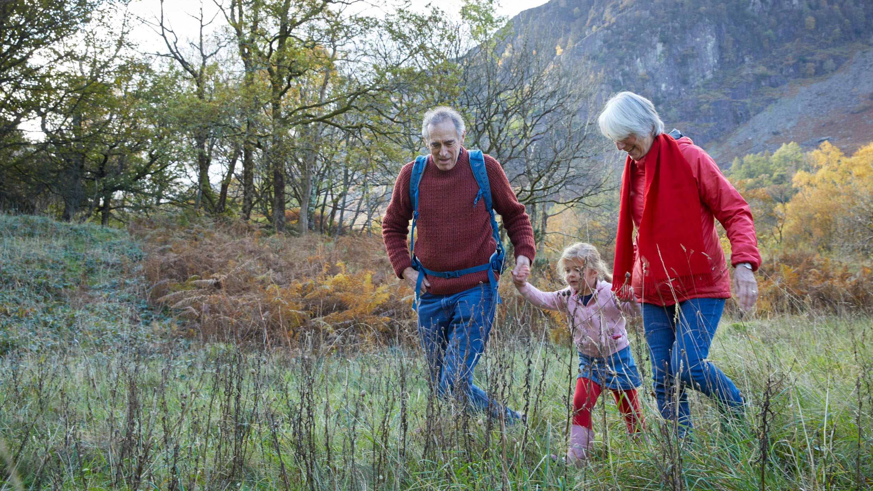 Three family members, including two adults and one young child, walk together holding hands in the countryside
