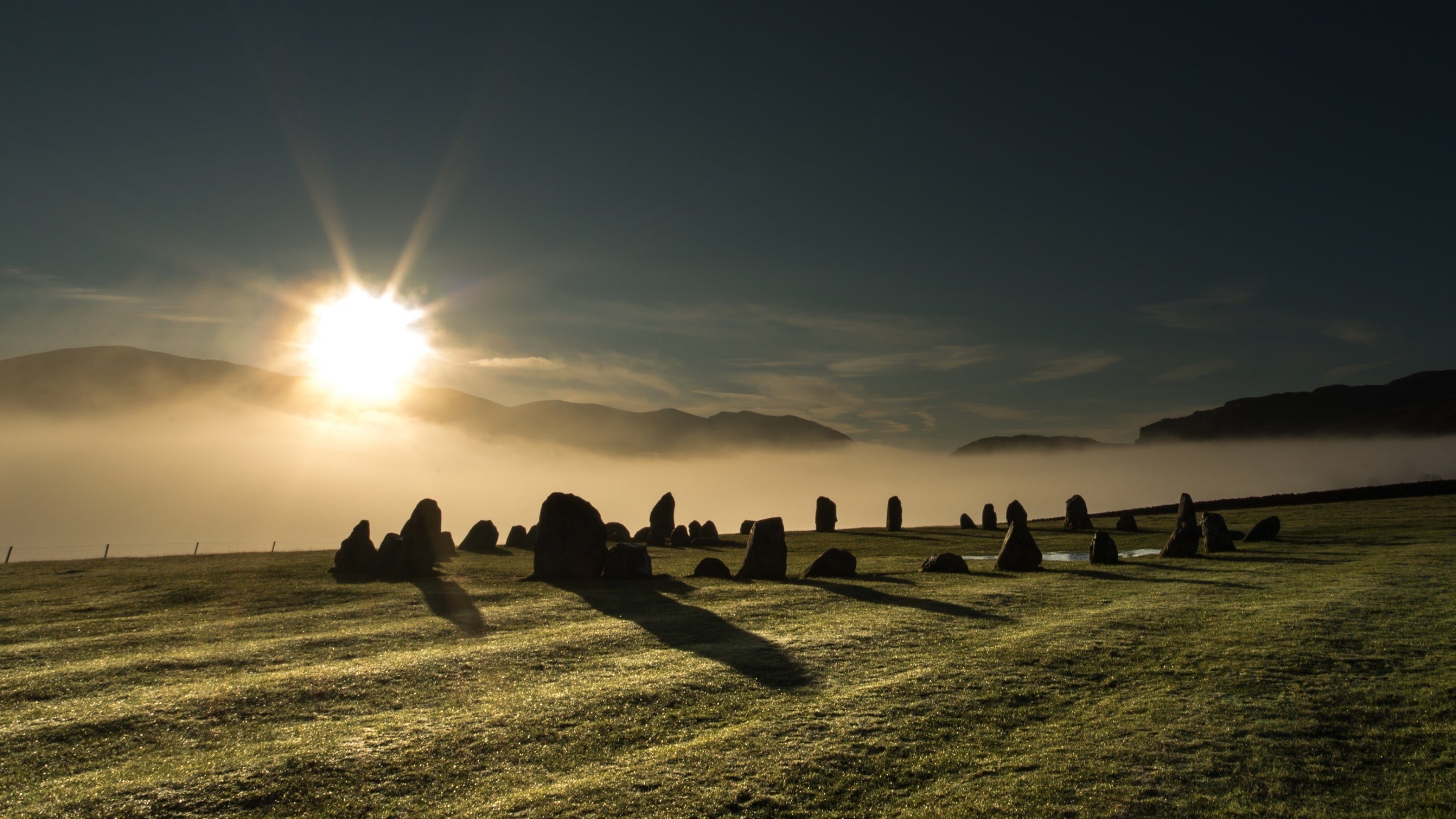 The sun rises over Castlerigg stone circle in winter, which is set against a backdrop of low cloud