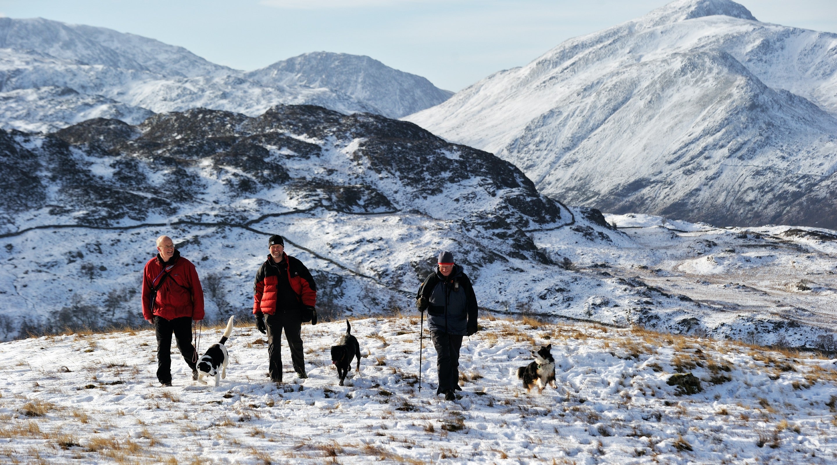 Walkers with their dogs hiking through the snow on the fells around Watendlath on a clear day.