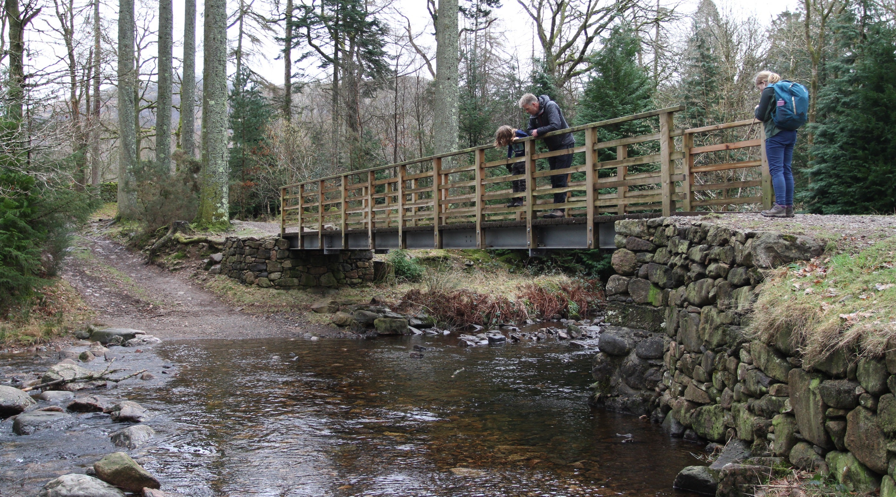A family play pooh sticks on a bridge while walking the River Esk trail on a cloudy winter's day