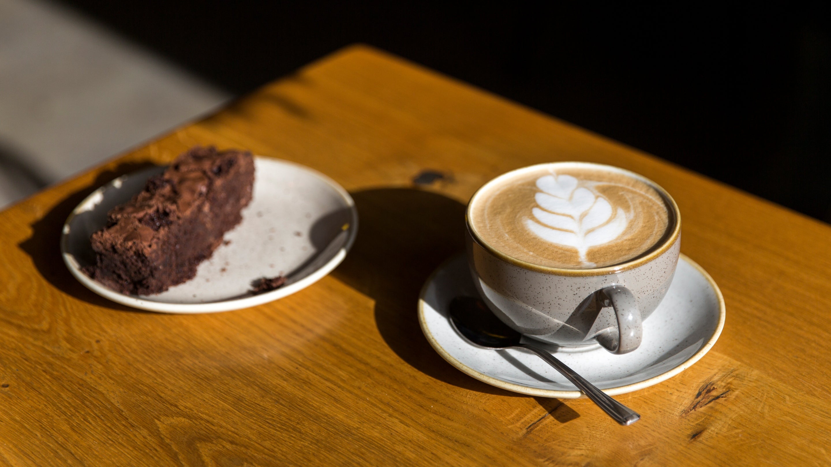 A piece of chocolate cake and a cup of coffee on a sunlit table