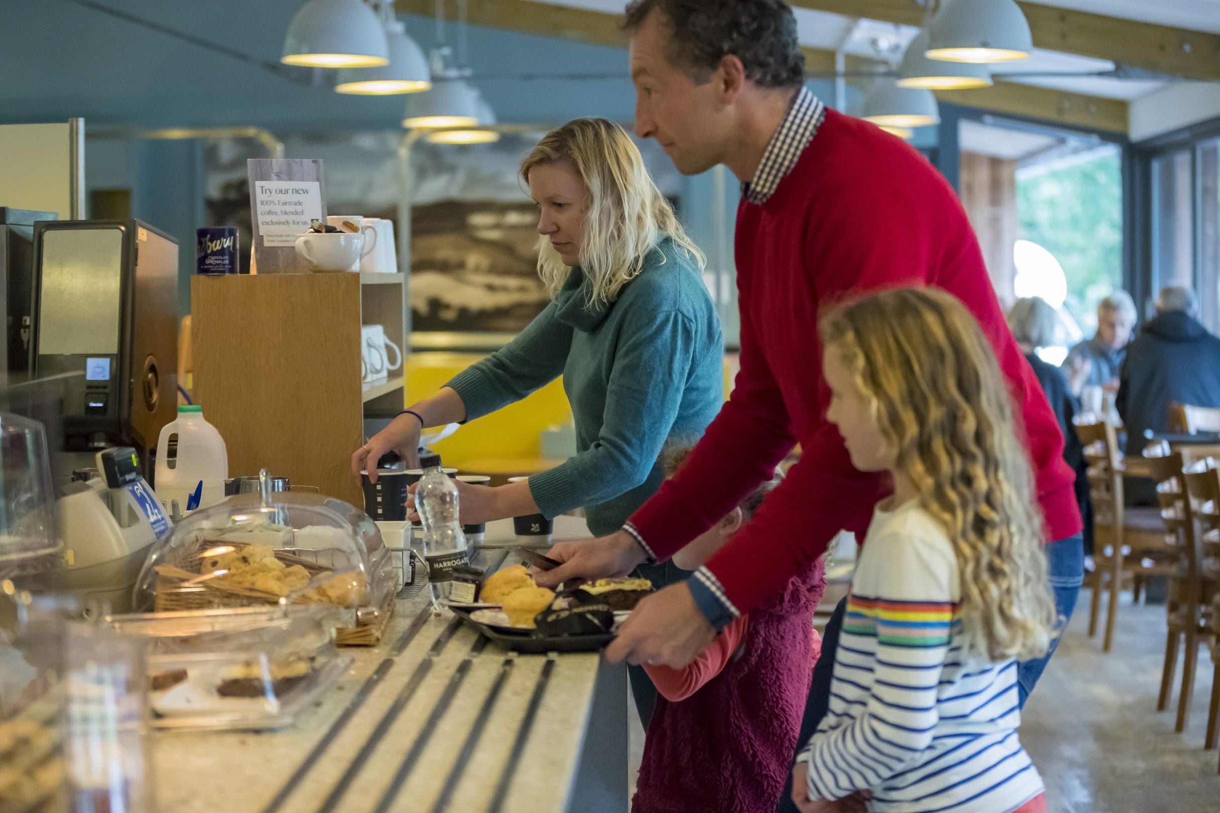 Mother, father and child paying at the cafe counter at Sizergh. They have a tray with two scones and a piece of cake.