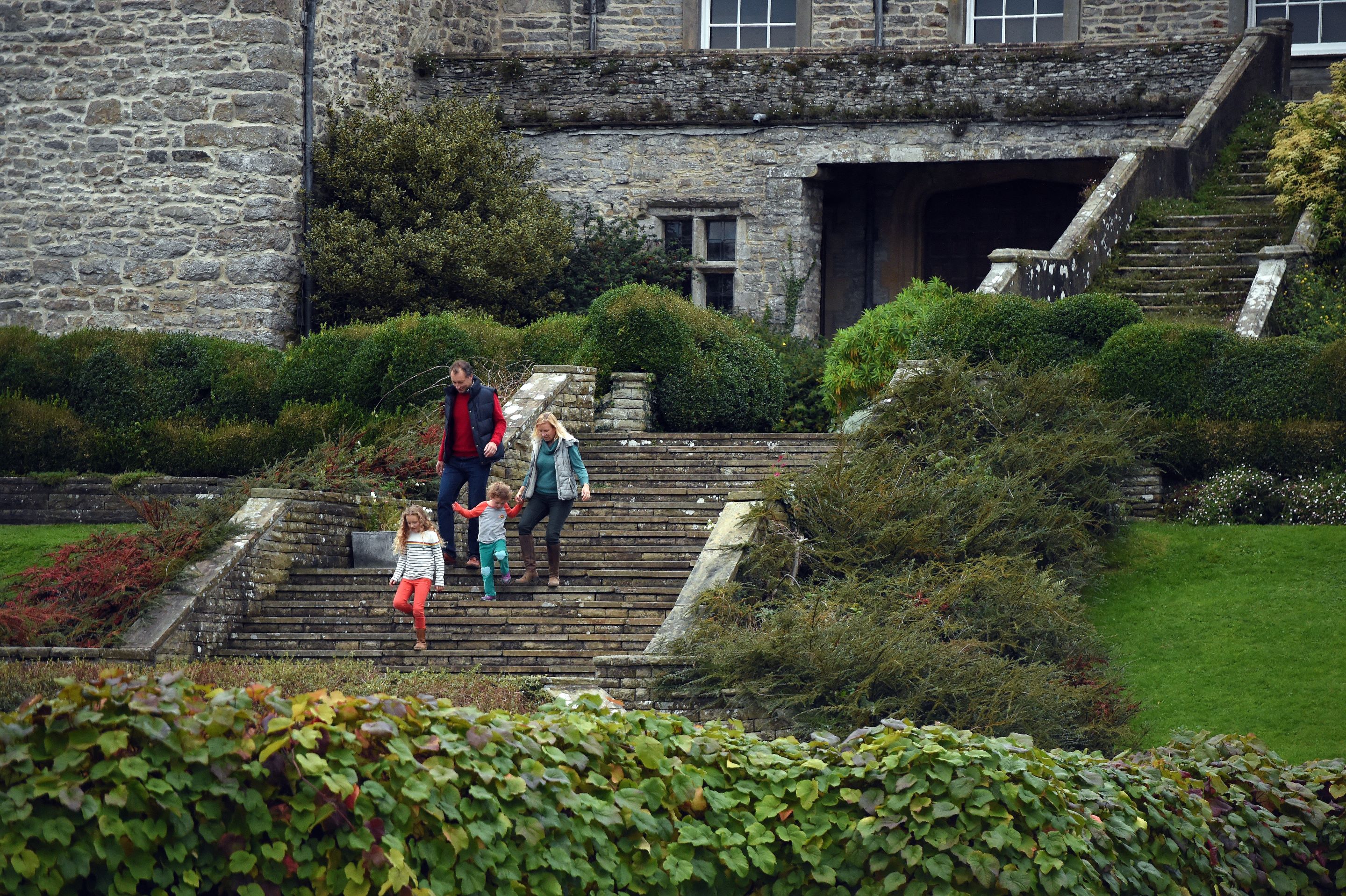 Family of four walking down the steps at the front of Sizergh Castle into the garden. The trees and leaves are red and orange.