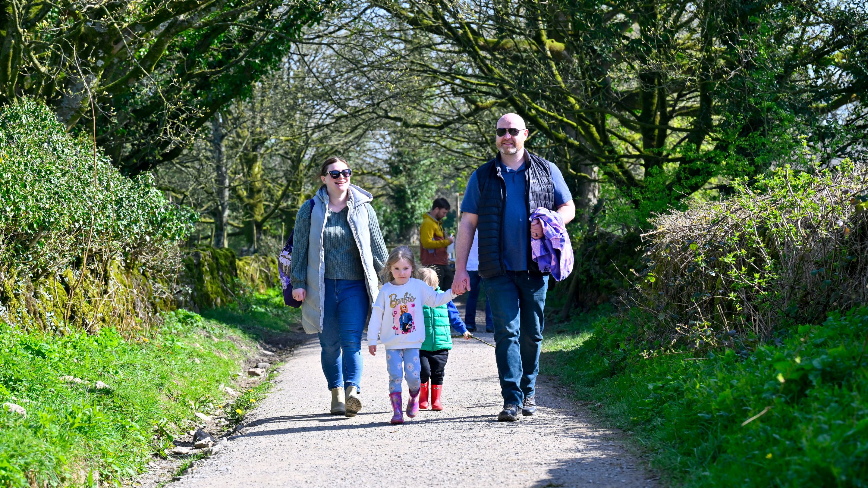 Adults and children walking along a tree‑lined path at Sizergh estate.