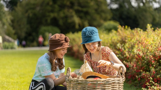 Two girls dressing up in the garden with 1920s hats on, smiling.