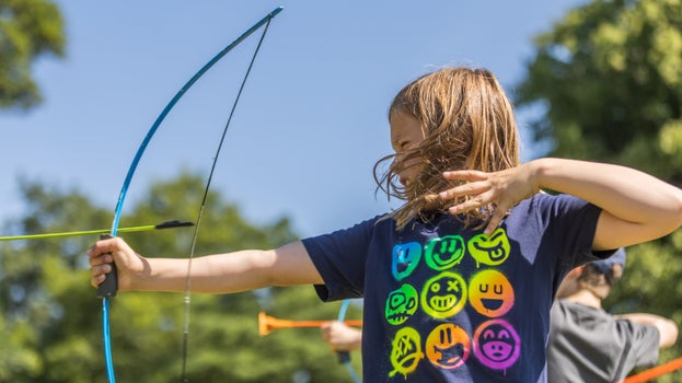 Child playing archery pulling back the bow in a field on a sunny day