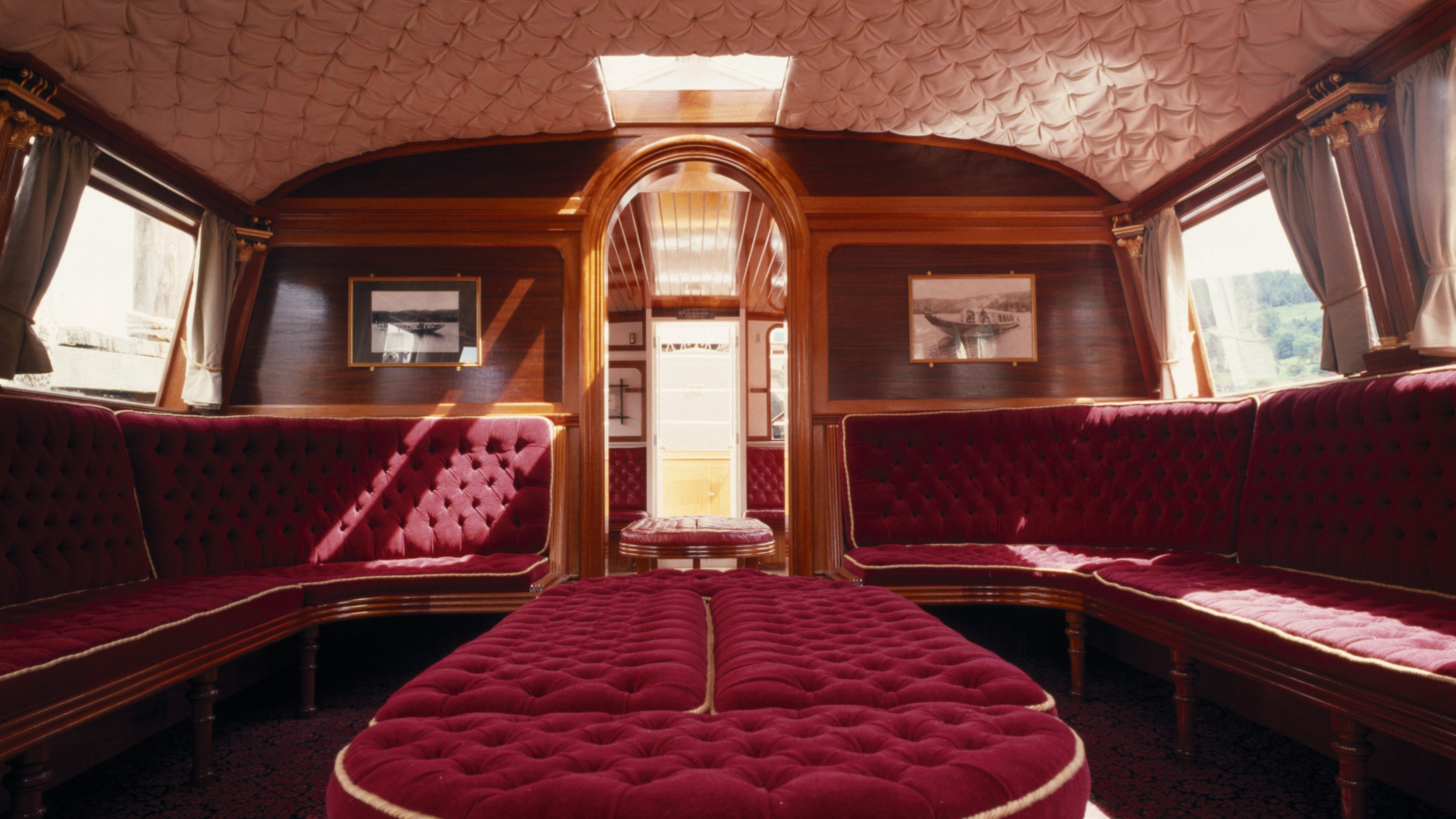 View of the restored interior of the Gondola on Coniston Water, Lake District, facing towards the stern of the boat, red velvet seating, and quilted ceiling.