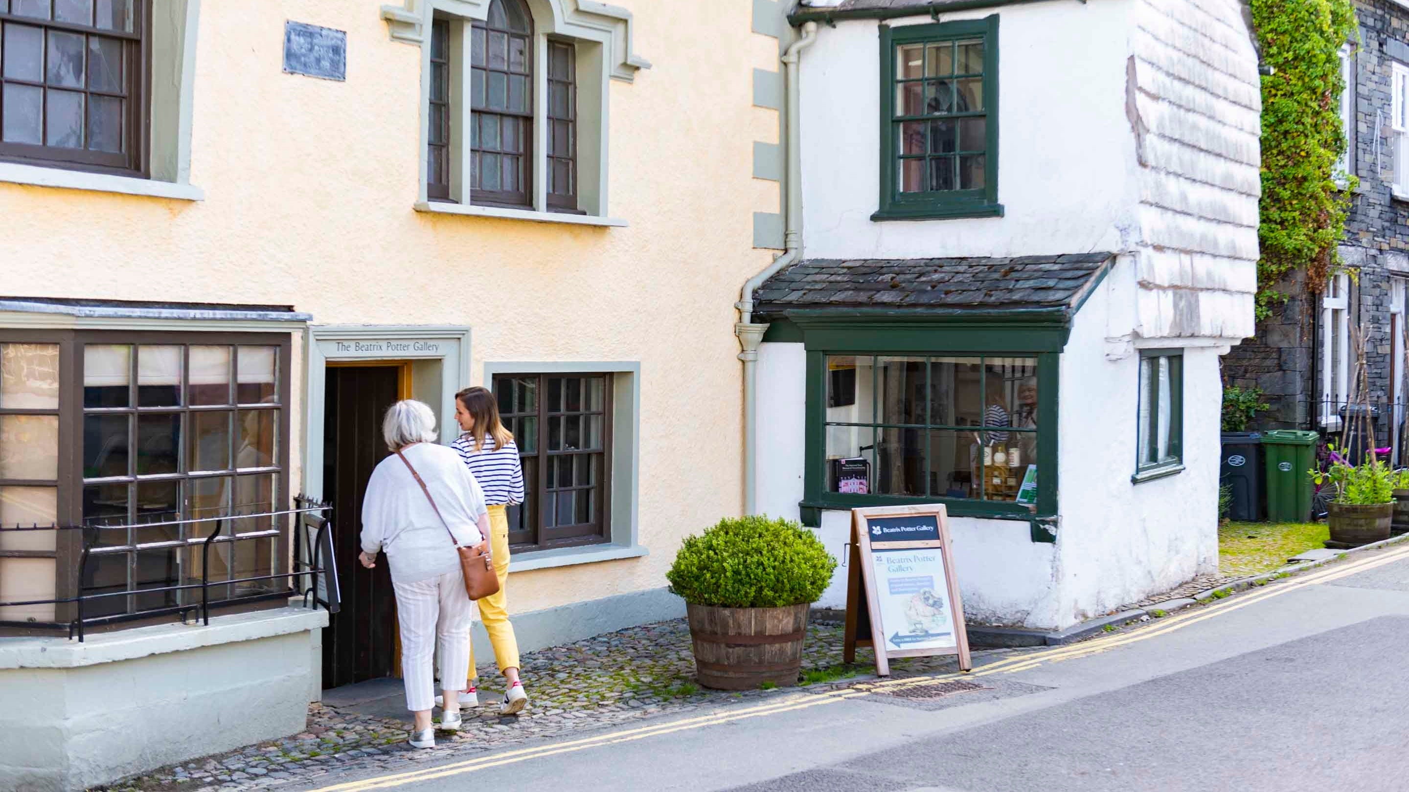 Two visitors walking through the doorway of the Beatrix Potter Gallery, Hawkshead