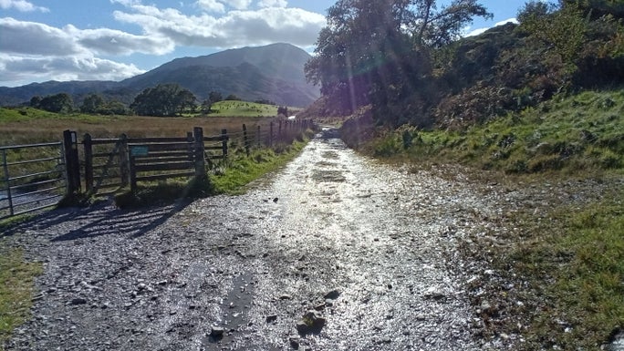 Loose gravel path with a field on one side and grassy banking on the other and views of the hills in the background, Little Langdale, Cumbria