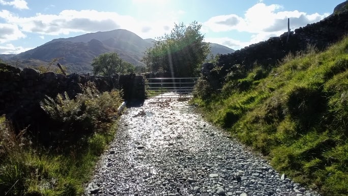 Loose gravel path with a drystone wall on one side and grassy banking on the other and views of the hills in the background, Little Langdale, Cumbria