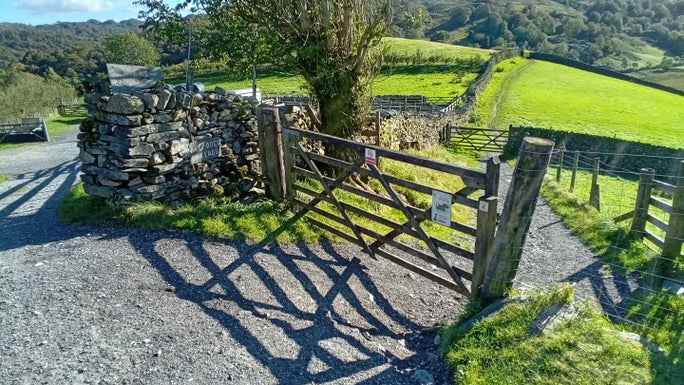A large wooden gate across a footpath which slopes steeply downhill, Little Langdale, Cumbria