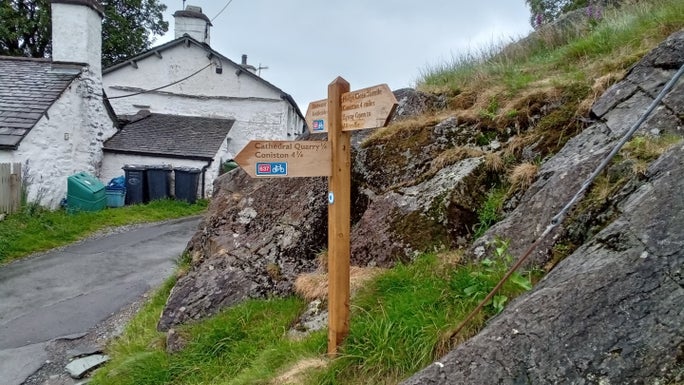 A wooden signpost with a white cottage in the background, Little Langdale, Cumbria