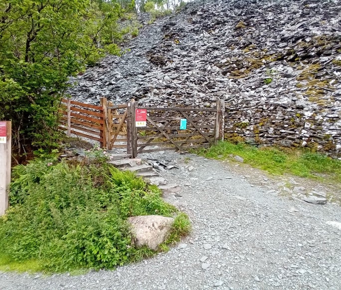 A stone footpath leading uphill to a wooden gate with large piles of stone in the background, Cathedral Quarry, Cumbria