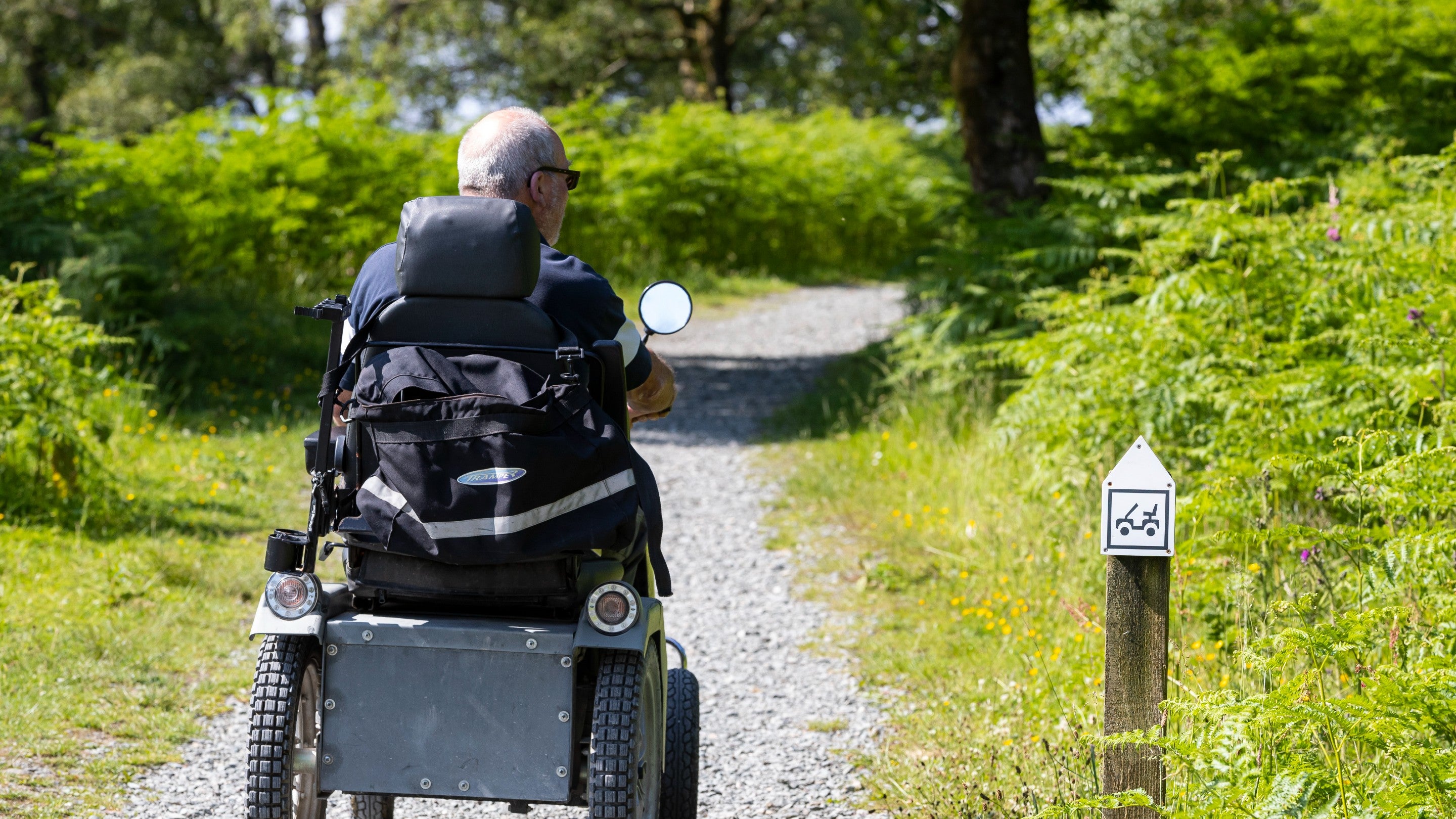 A visitor on a Tramper rides away down a gravel path at Tarn Hows and Coniston in Cumbria in the summer